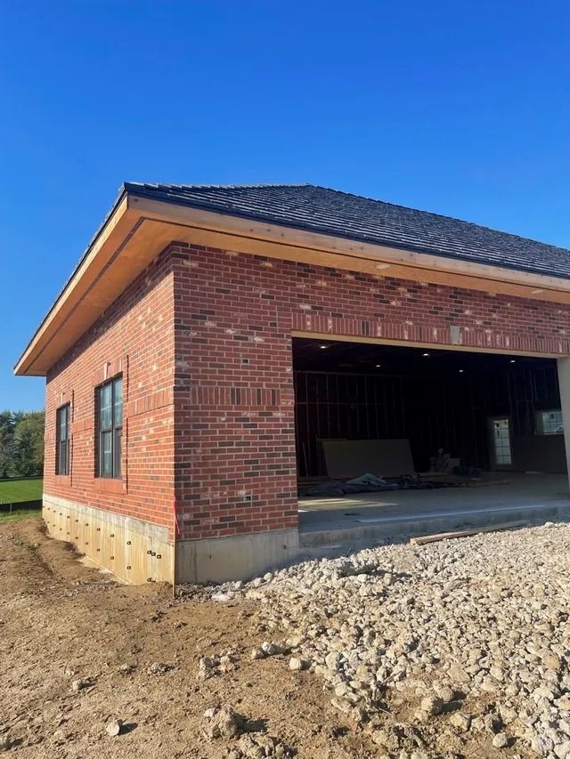 Red brick house with brown roof and beige window frames, next to a paved driveway.
