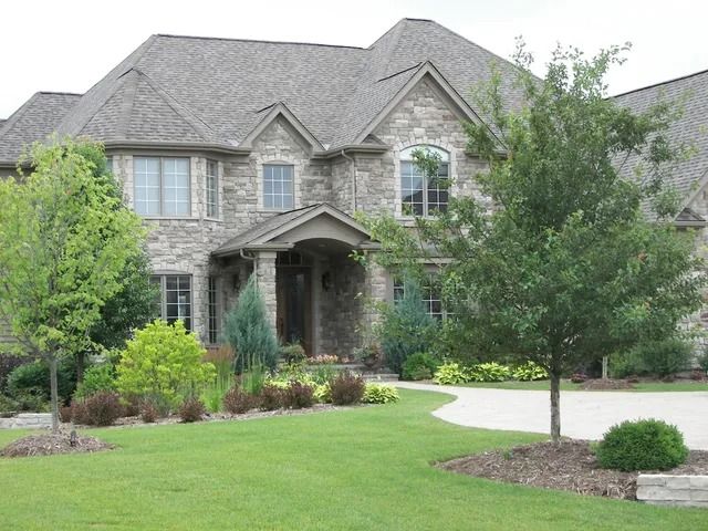 Gray house with white trim, stone accents, and a front porch under a clear sky.