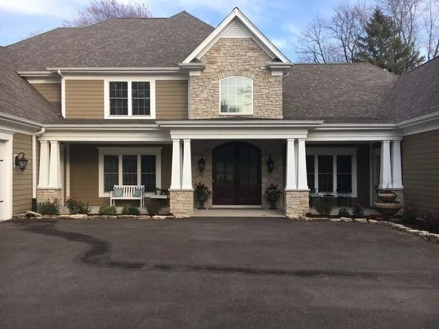 White house with stone base under construction on a dirt lot. Black window frames.
