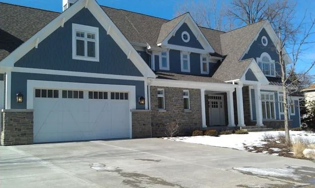 Stone facade of a new house with a white framed window. Brown trim, light-colored siding, and a cloudy sky.