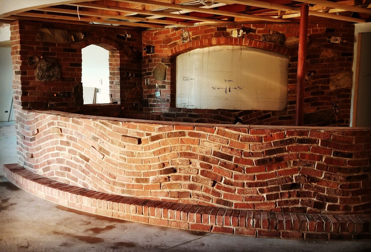 Brick bar under construction, with a curved facade and arched openings, interior setting.