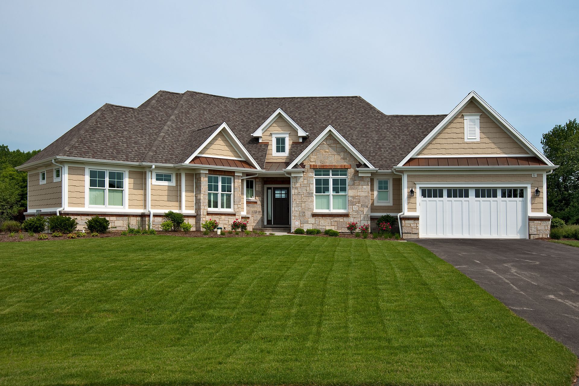 House with brick and siding, green lawn, driveway, and blue sky.