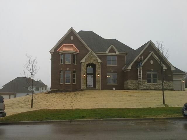 Brick house with stone accents on a cloudy day. Empty lawn in front; small tree on left.