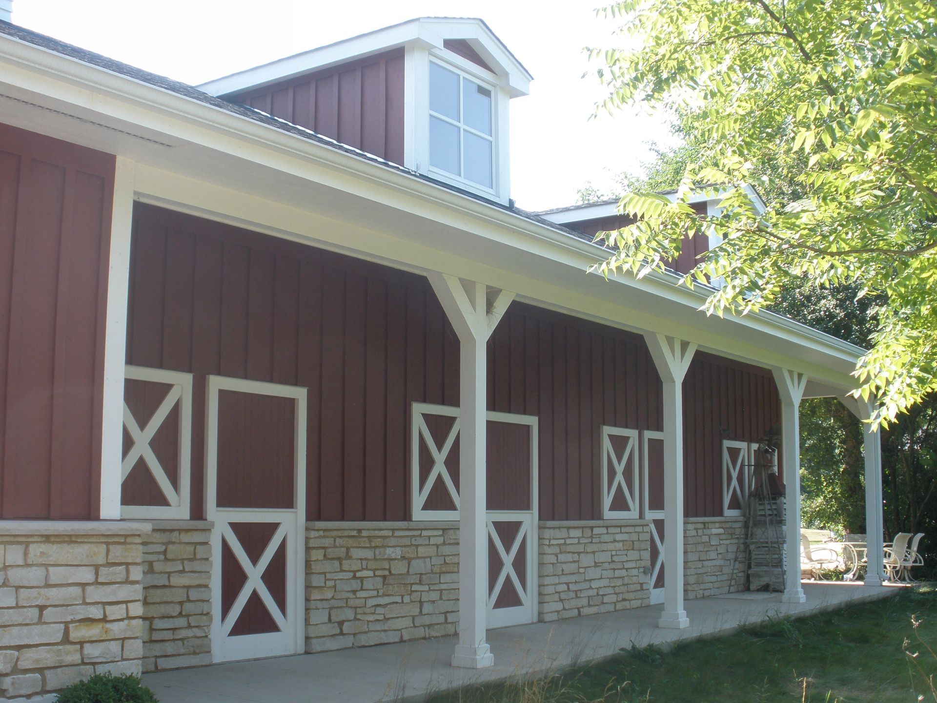 Red barn with white doors and pillars, beige stone foundation, and a small upper window.