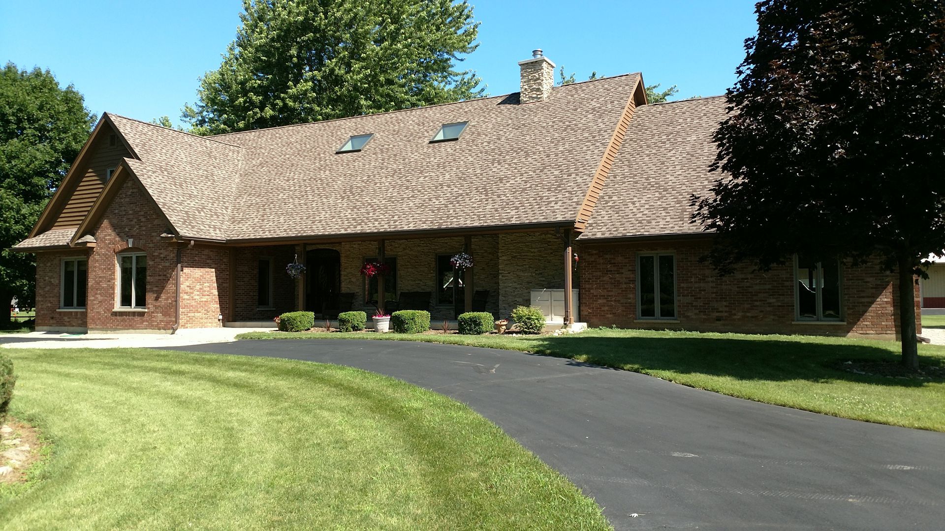 Brick house with brown roof, green lawn, and black driveway under a blue sky.