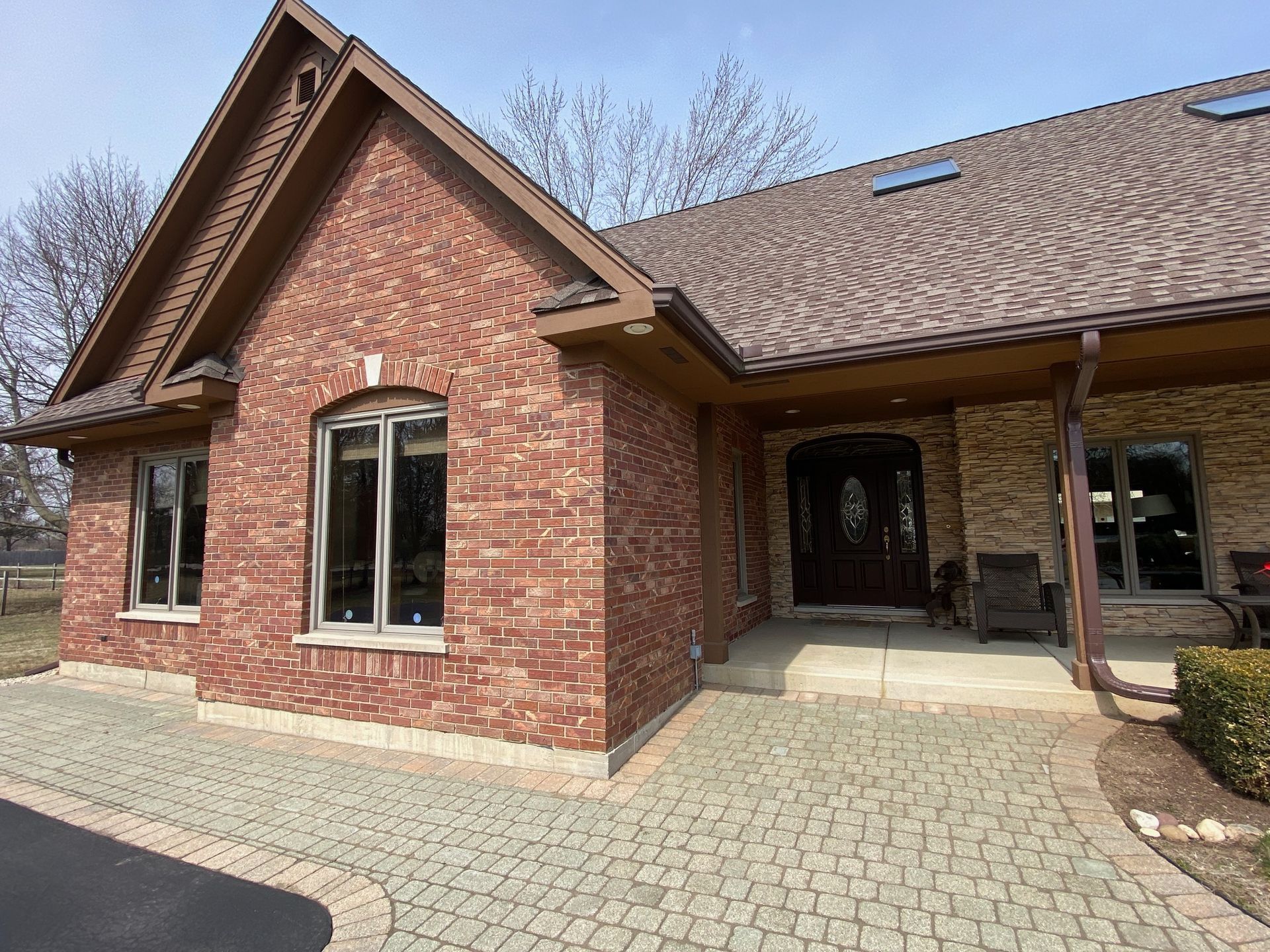 Brick house with brown roof, windows, and paved walkway. Sunny day.
