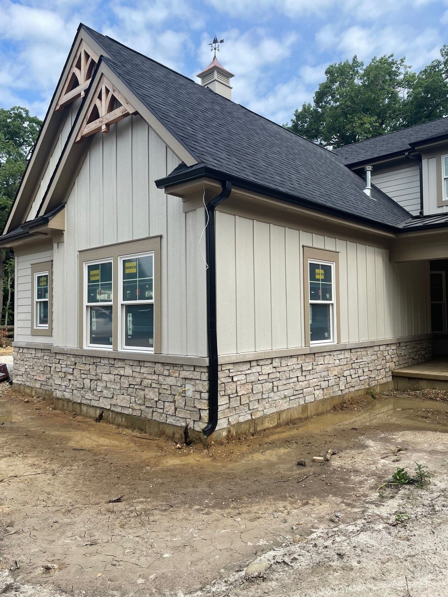 New construction house exterior with beige siding, stone base, black roof, and windows.