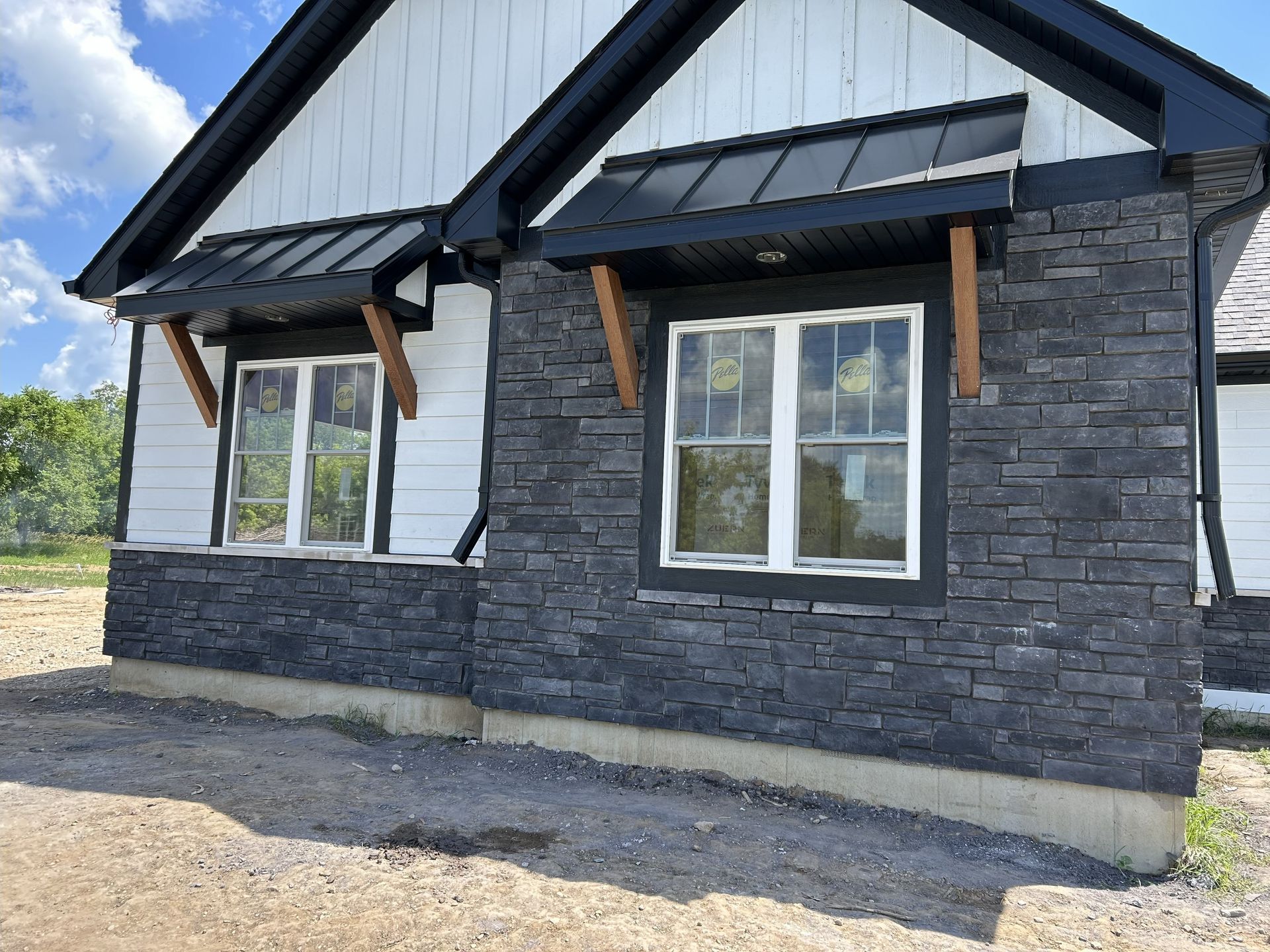 House exterior with dark stone siding, white trim windows, black awning, and wooden supports.