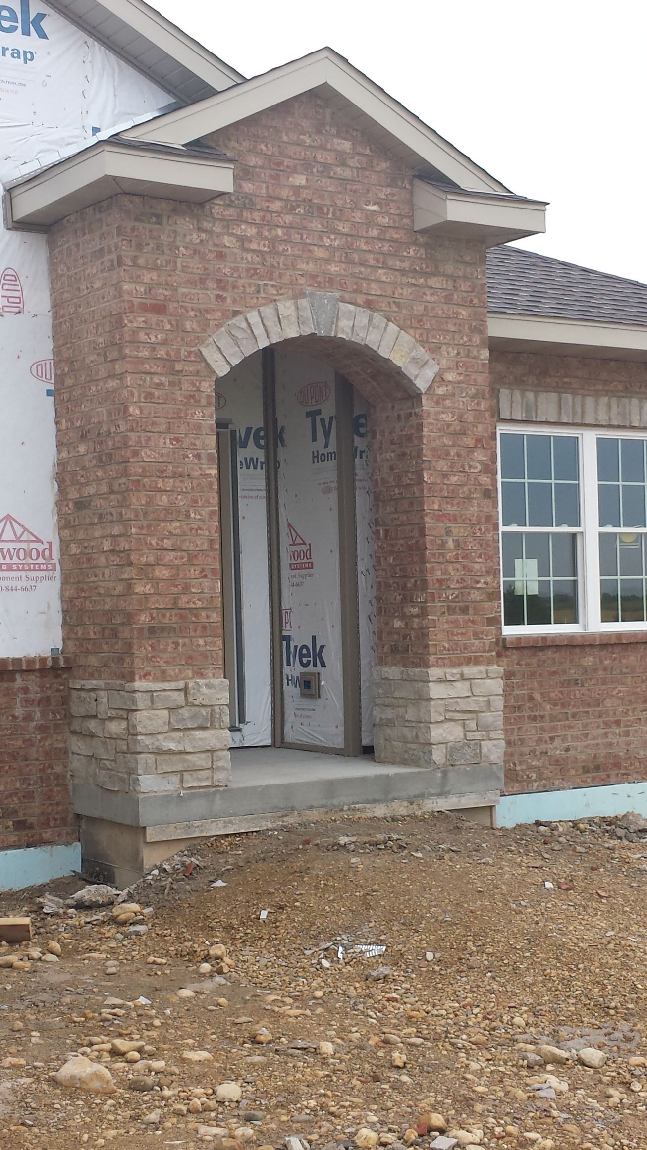 Exterior of a house under construction. Brick entryway with an arched top, a stone base, and a concrete step.
