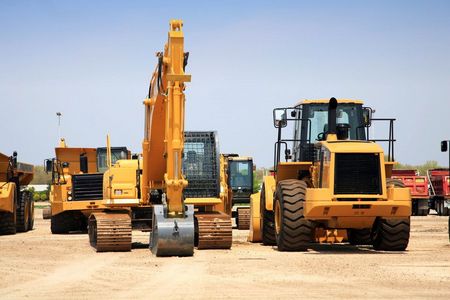 A group of yellow construction vehicles are parked in a dirt lot.