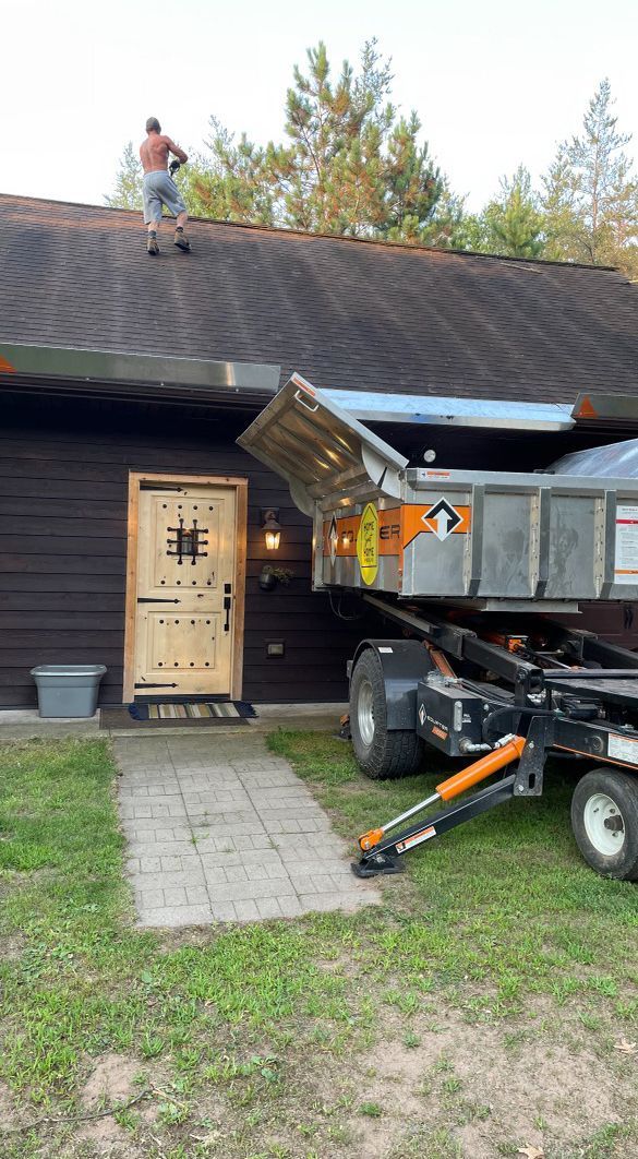 a man is standing on the roof of a house next to a dumpster