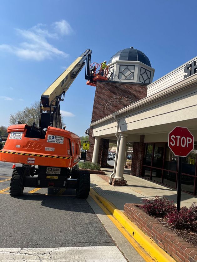 Orange crane truck lifting near a building with a domed roof and a stop sign in front
