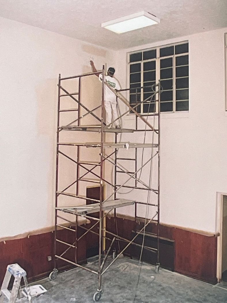 Worker on scaffold painting a room.