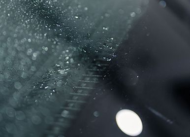 Raindrops on a car windshield, blurry background, with a bright white light and dark reflections.