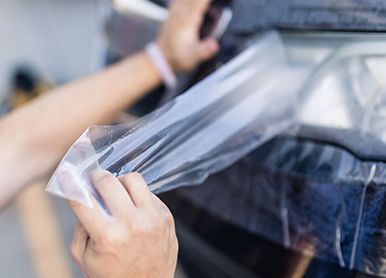 Person peeling protective film from a car's headlight.