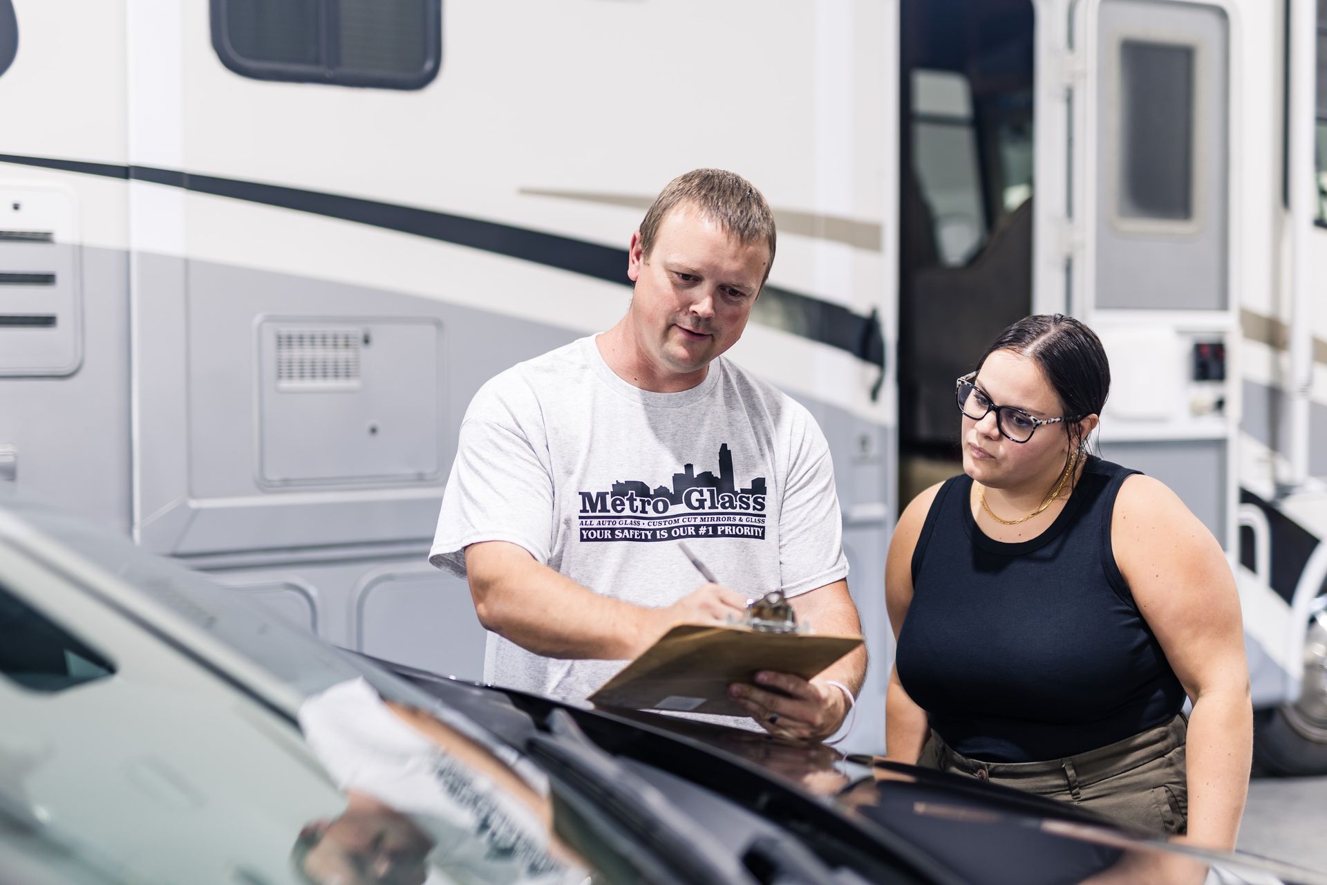 Man and woman reviewing a clipboard next to a motorhome, likely discussing details. They are outside in a sunny area.