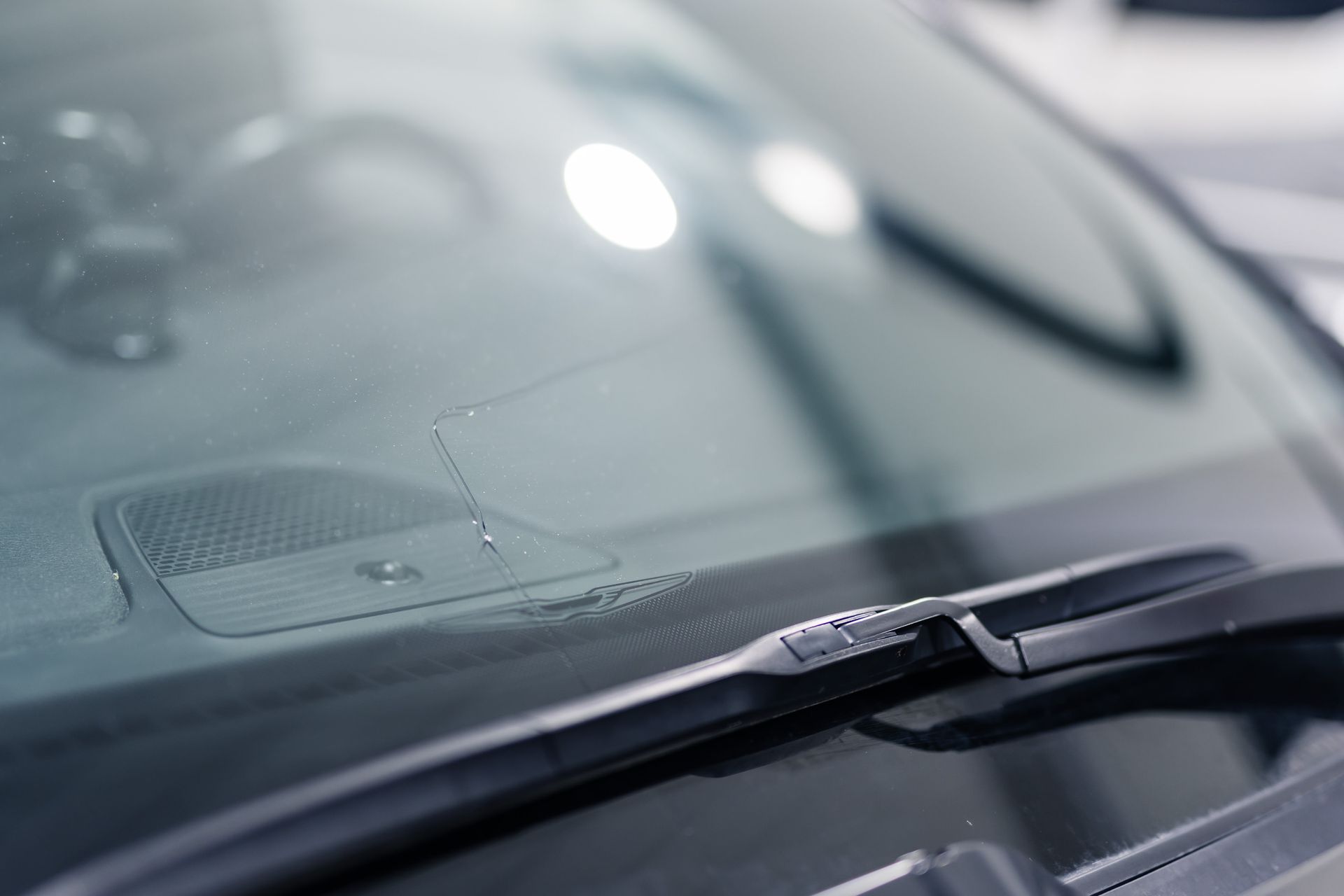 Close-up of a car windshield with a crack, wiper blade in view, and light reflections.