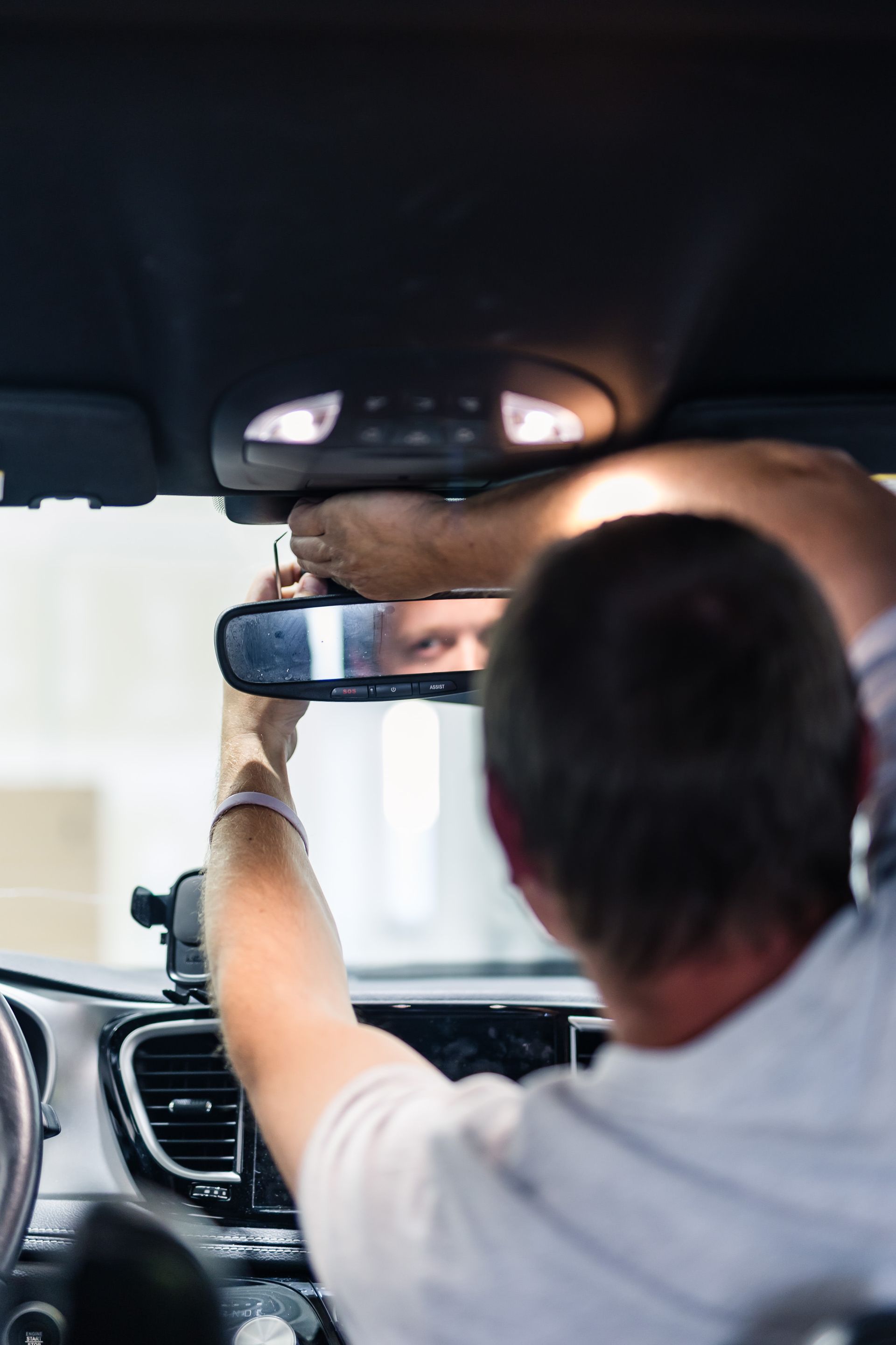Person adjusting a rearview mirror inside a car. They are reaching up with their hands towards the mirror under the car's interior lights.