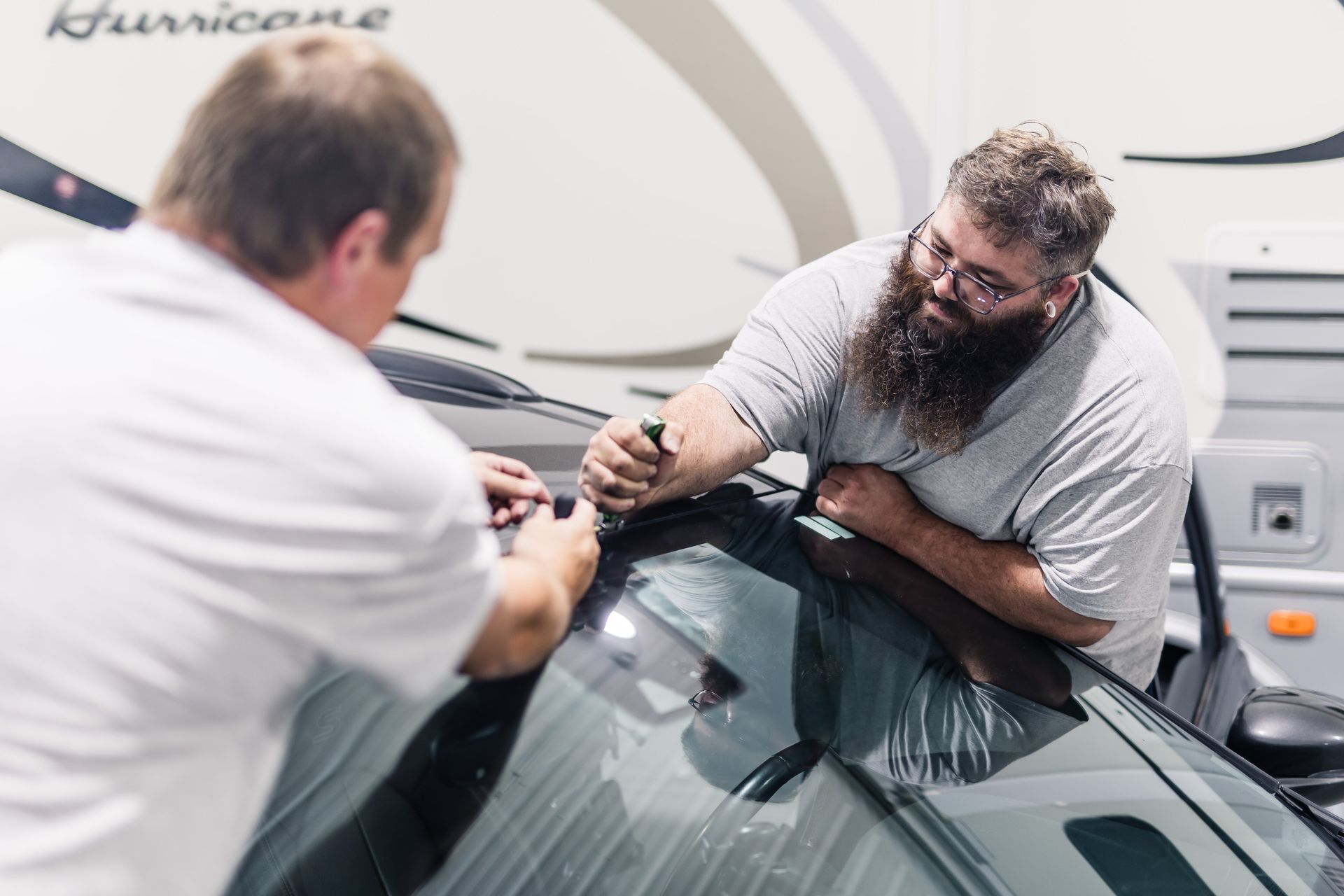 Two men installing tint on a windshield of a vehicle. One man is using a tool while the other assists.