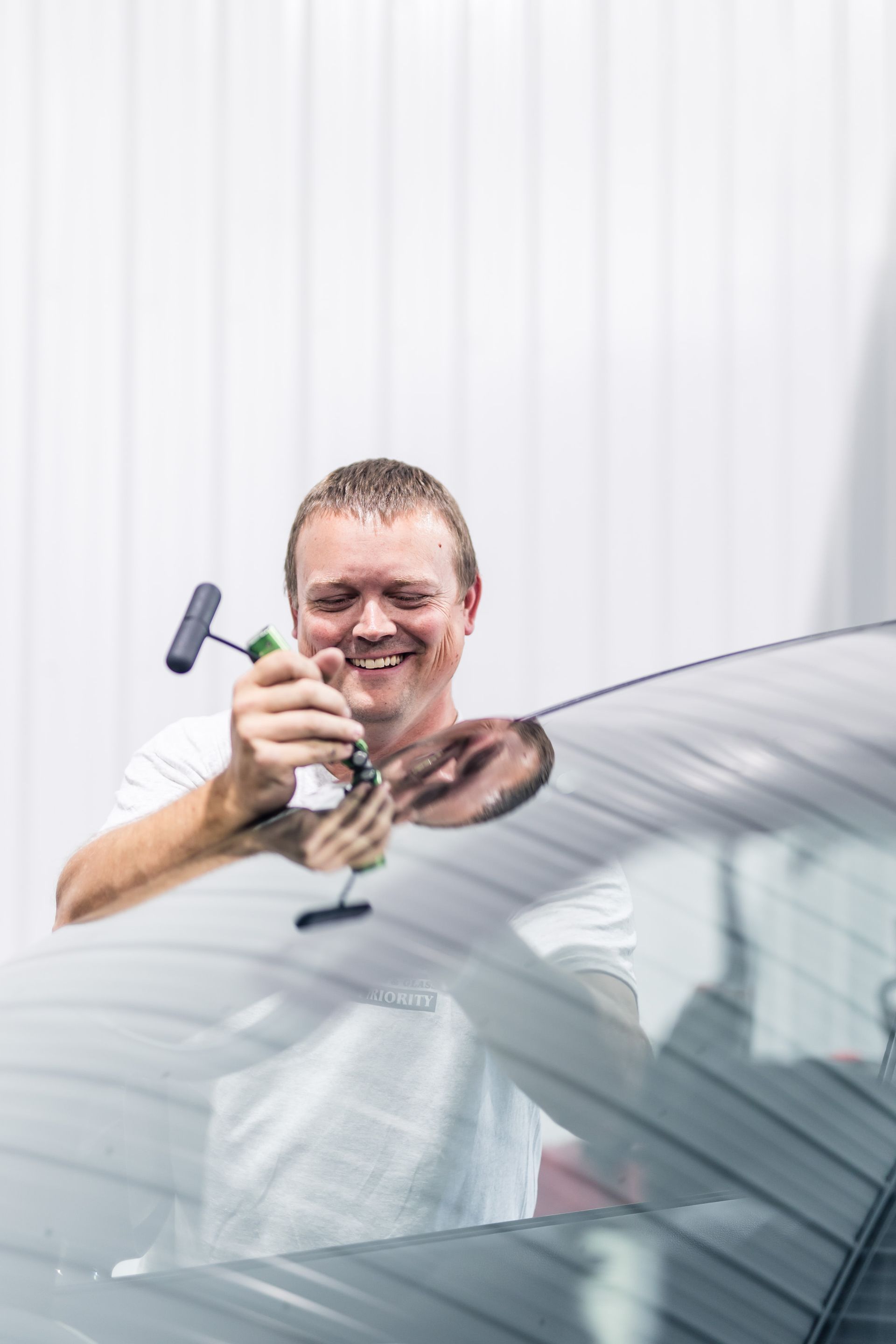 Man smiles while cleaning a car's windshield with a squeegee, white building in the background.