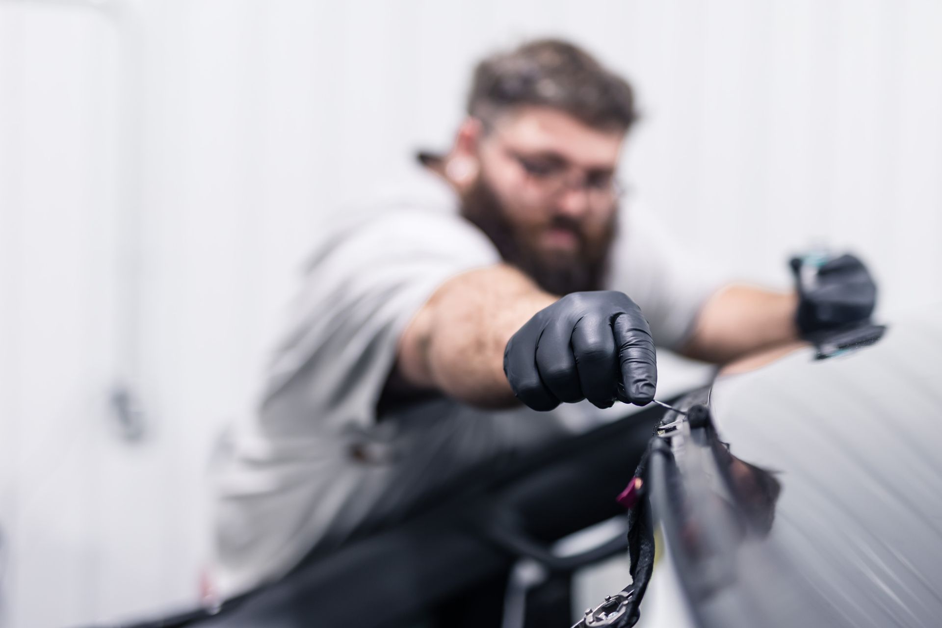 Man in black gloves working on a car, blurred background in a white room.