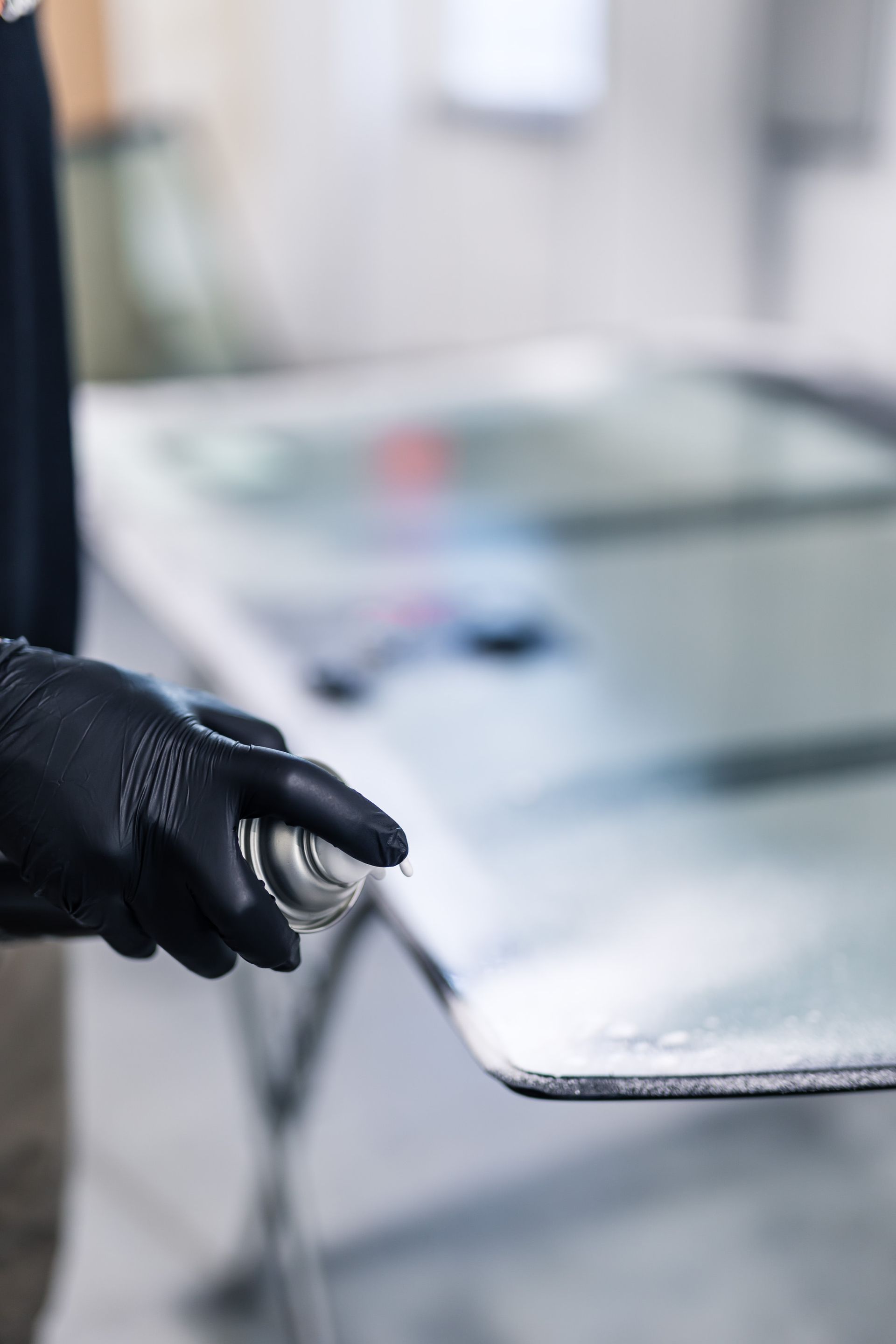 Gloved hand spraying cleaner onto a windshield in a workshop.