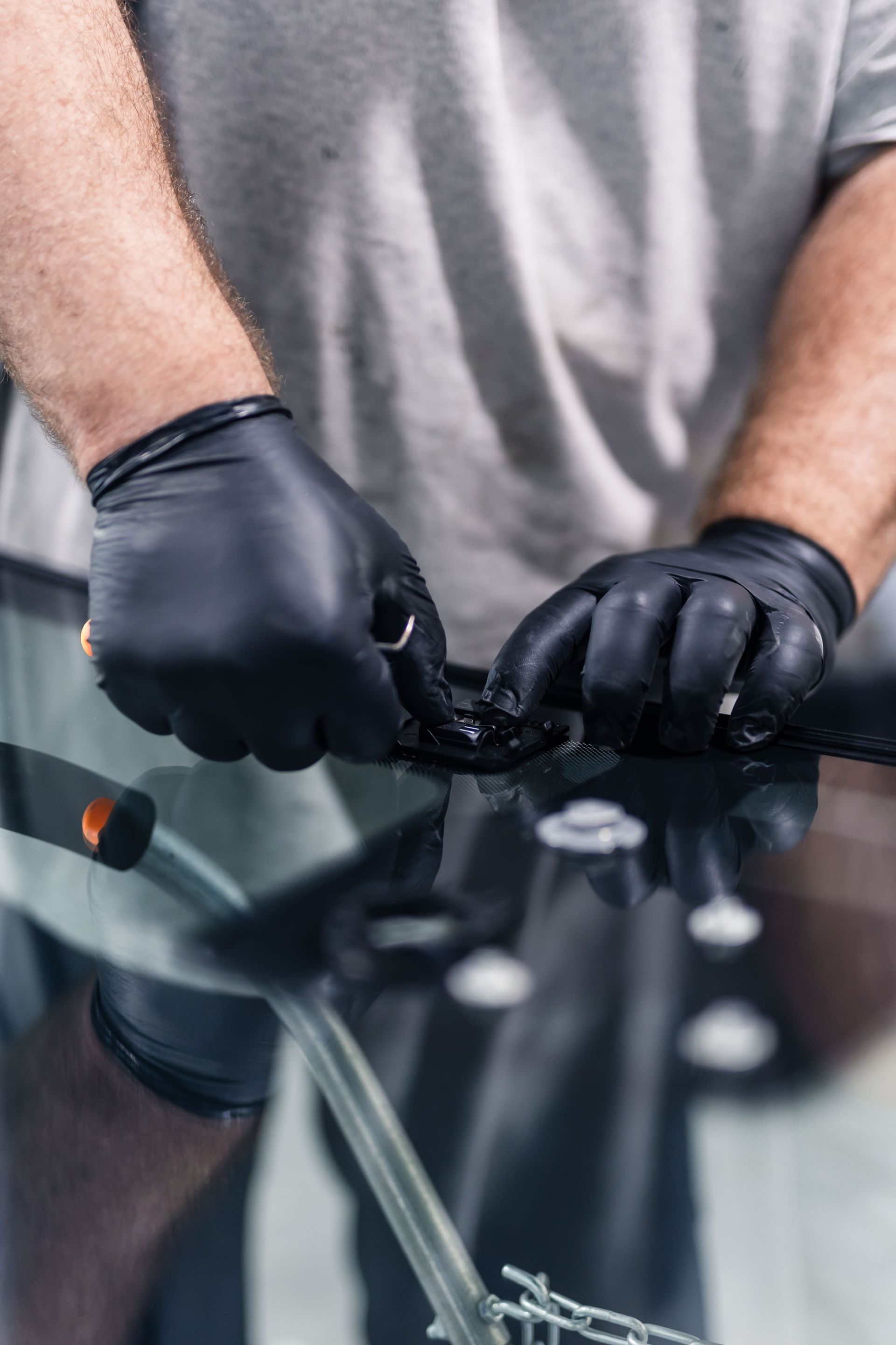Person in black gloves working on a car's windshield, likely replacing it. Focus on hands and the windshield.