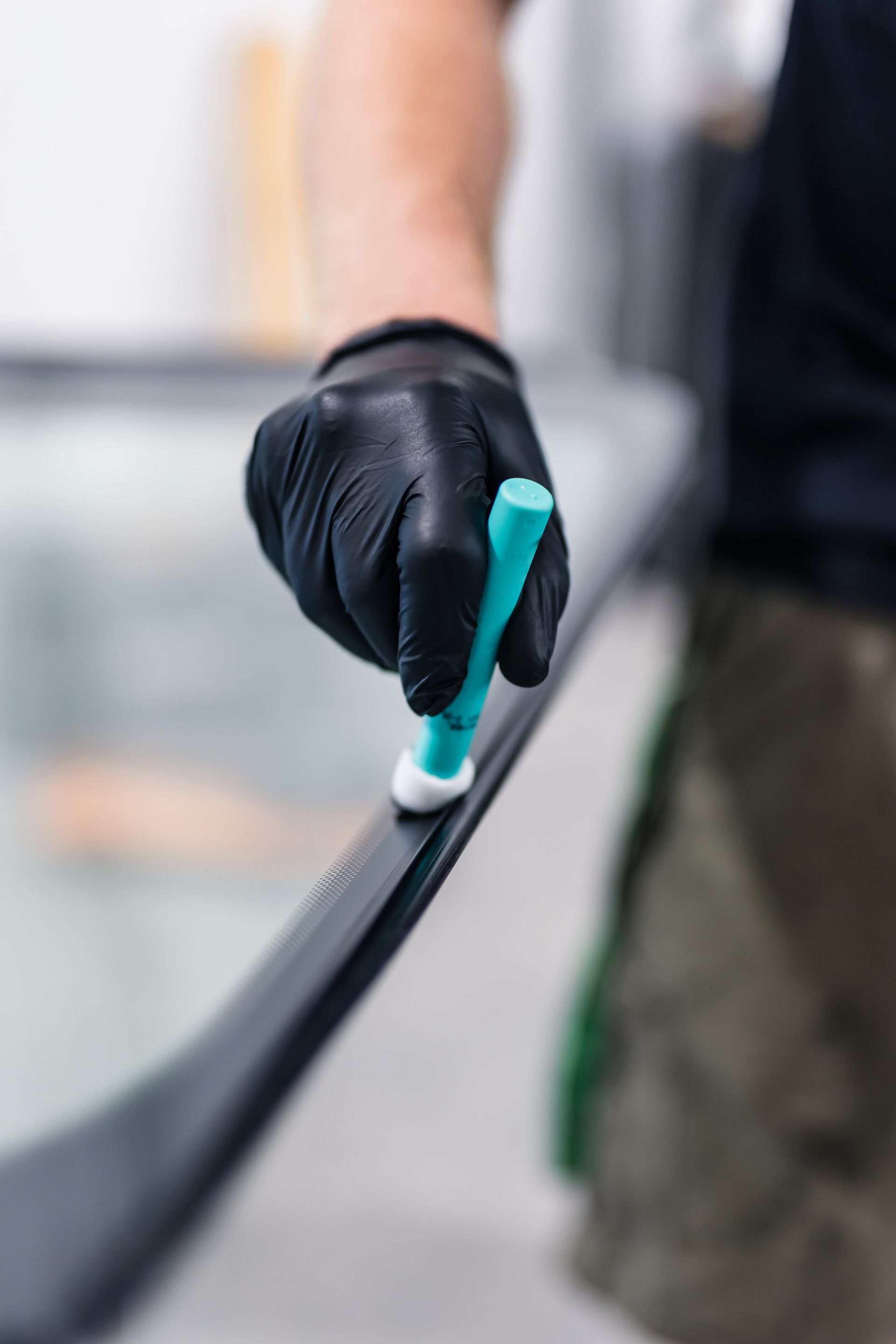 Person wearing a black glove applies a white substance to a black surface with a blue applicator.