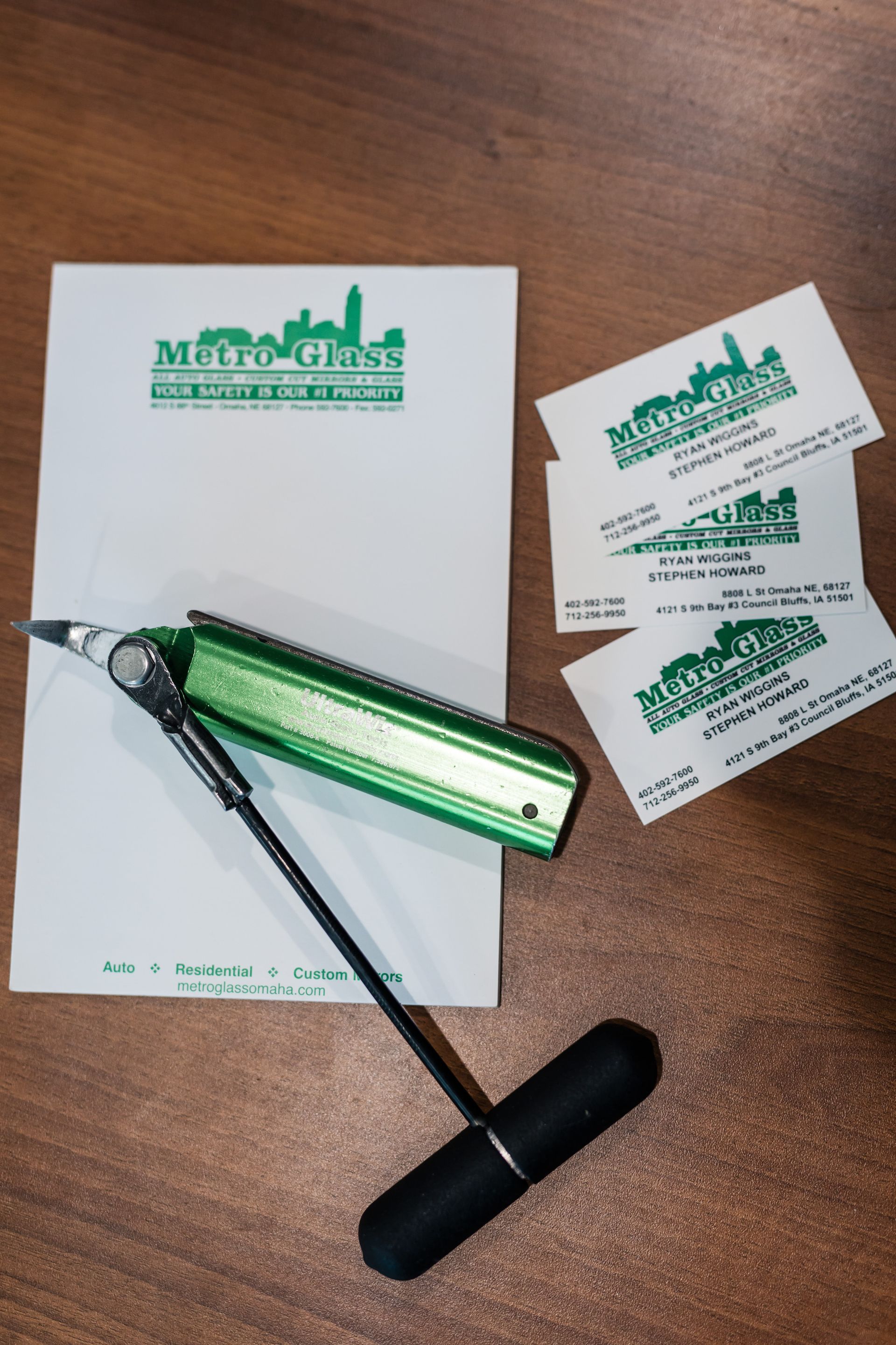 A green pen, business cards, and notepad with a green logo of a cityscape sit on a wood surface.