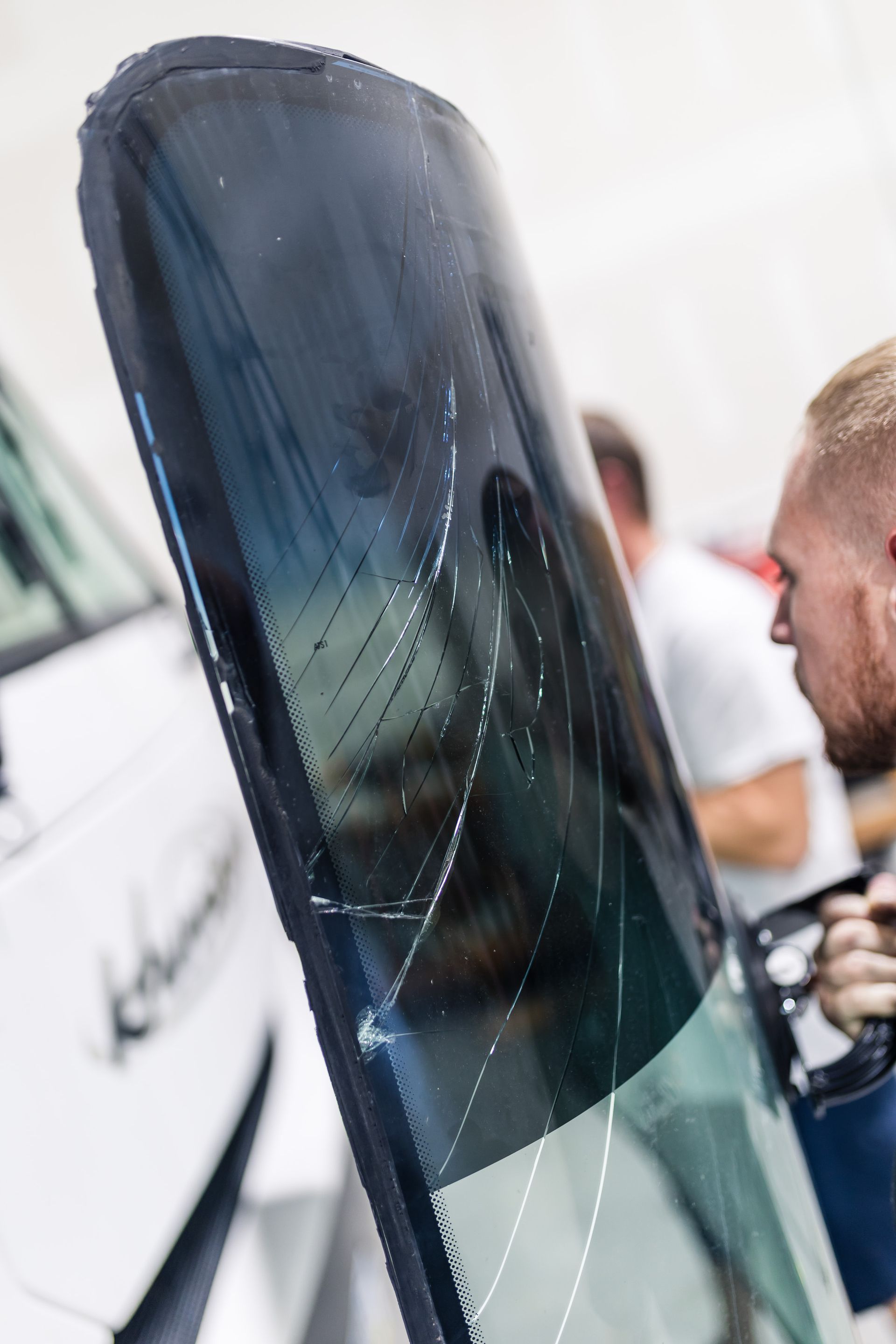 Person holding a car windshield with visible cracks, likely damaged and being replaced.