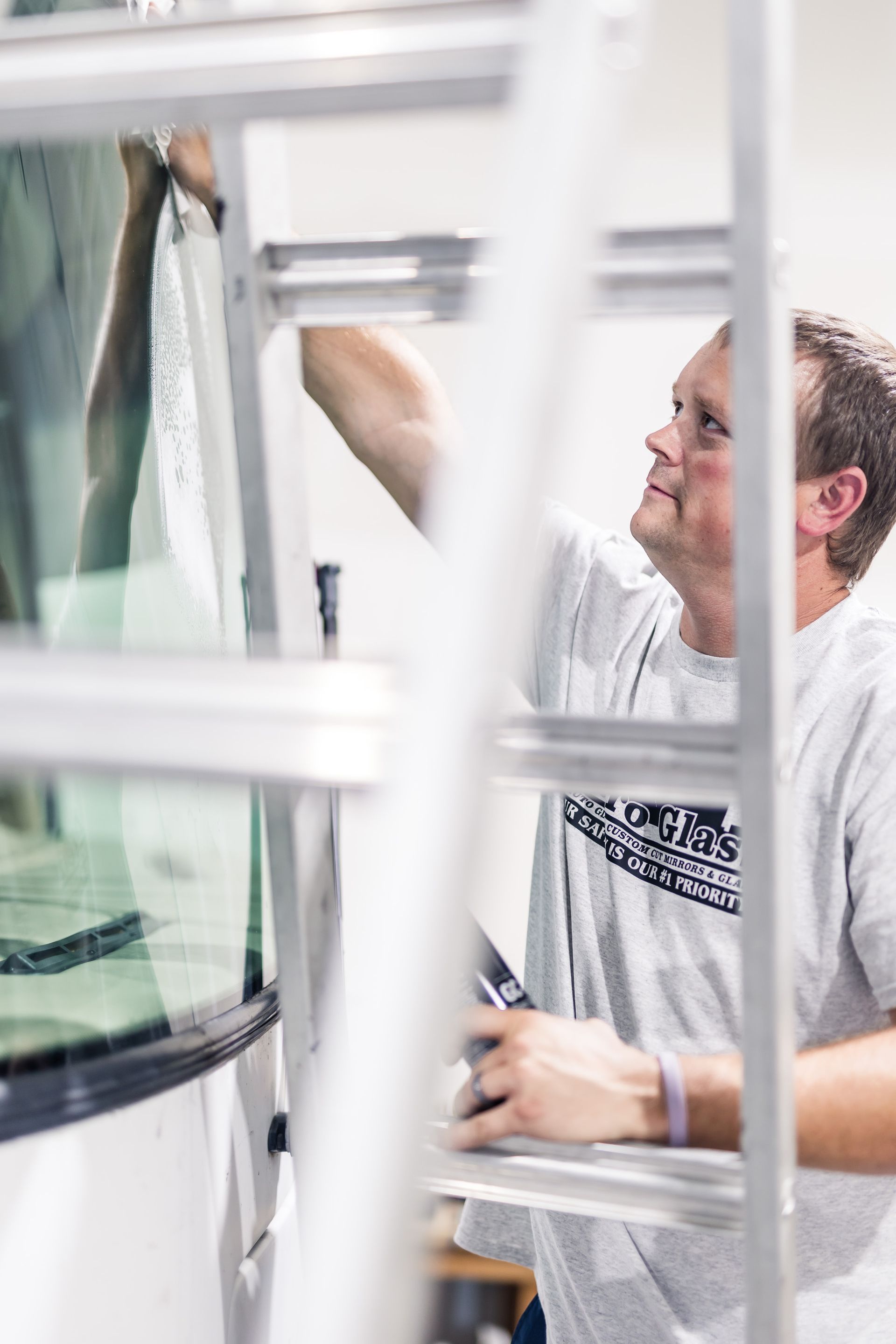 Man applying window tint while standing on a ladder. He is in a white shirt and looking up.