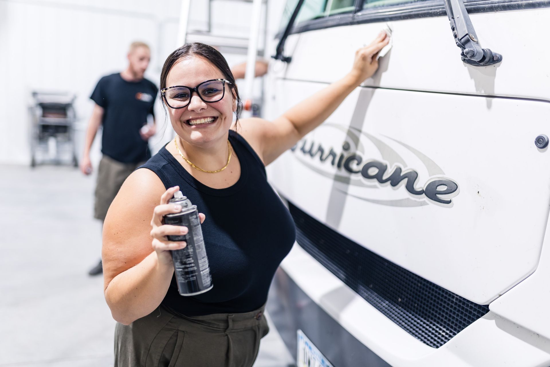 Woman smiling, spraying a white RV side panel labeled 