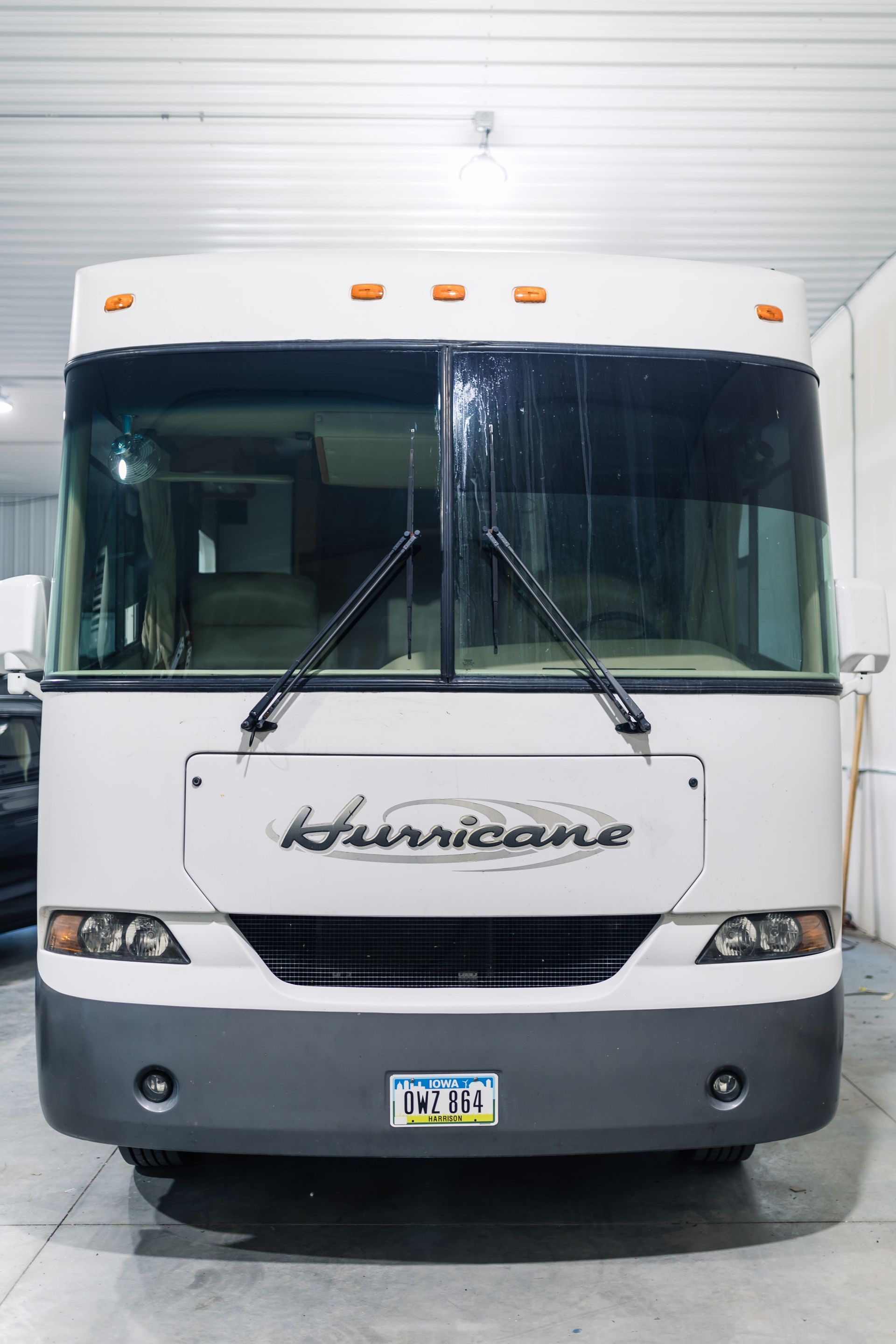 White and gray Hurricane RV, parked inside a garage. Front view showing windshield, headlights, and license plate.