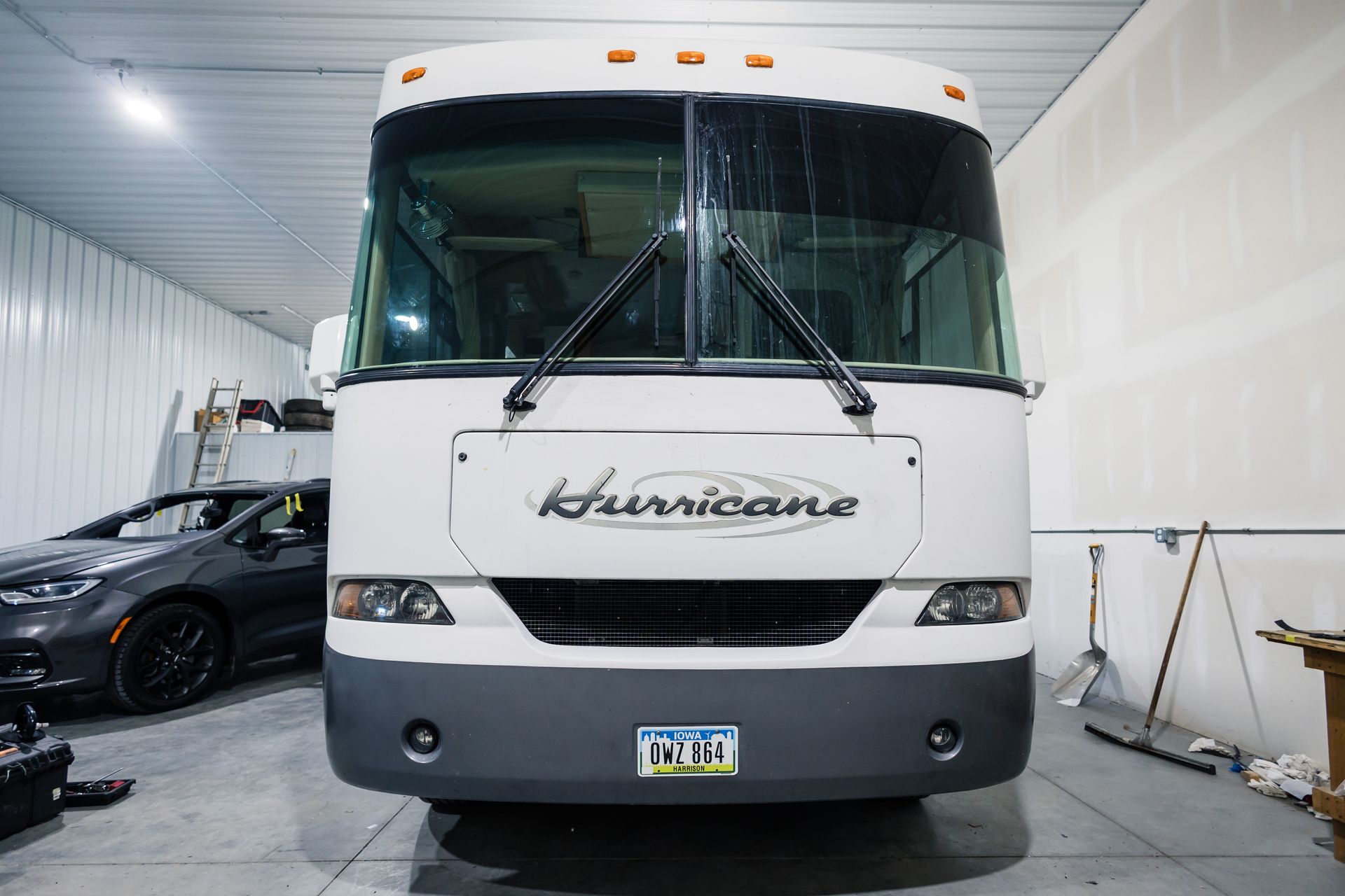 Front view of a white Hurricane RV parked in a garage; a gray sports car is visible to the left.