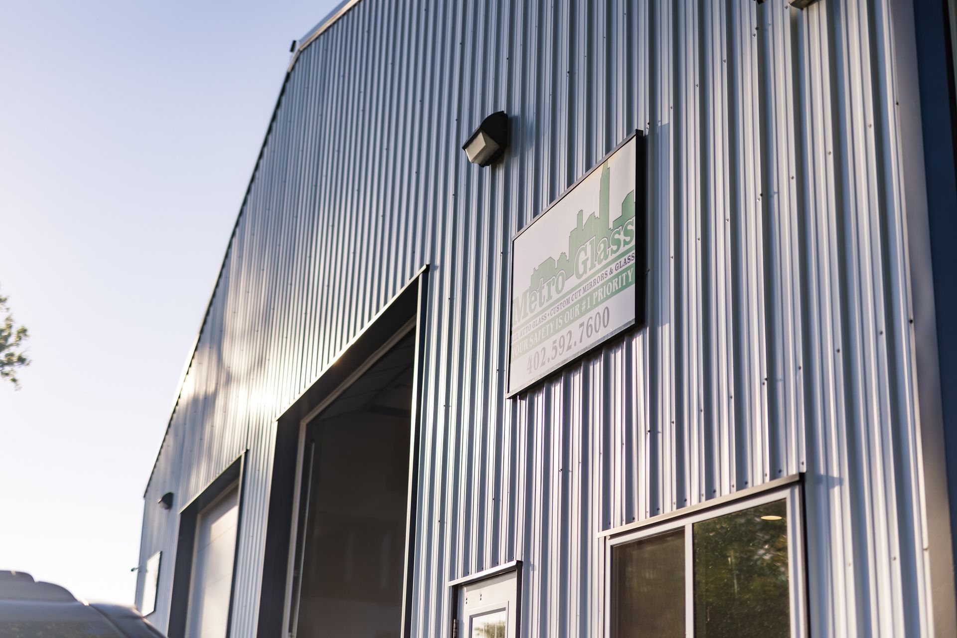 Exterior of a corrugated metal building with an open bay door and a sign. The sign is green with a city skyline outline.