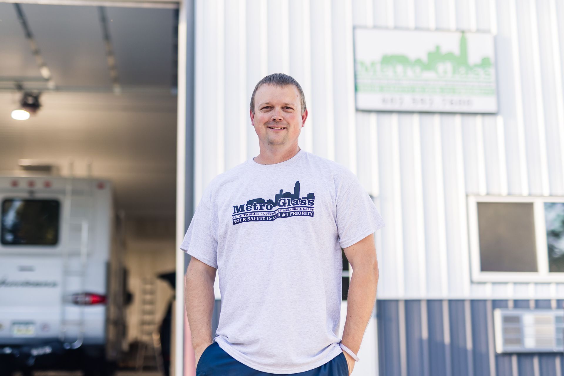 Man standing in front of a building with a sign and RV inside. He's wearing a t-shirt with a city skyline.