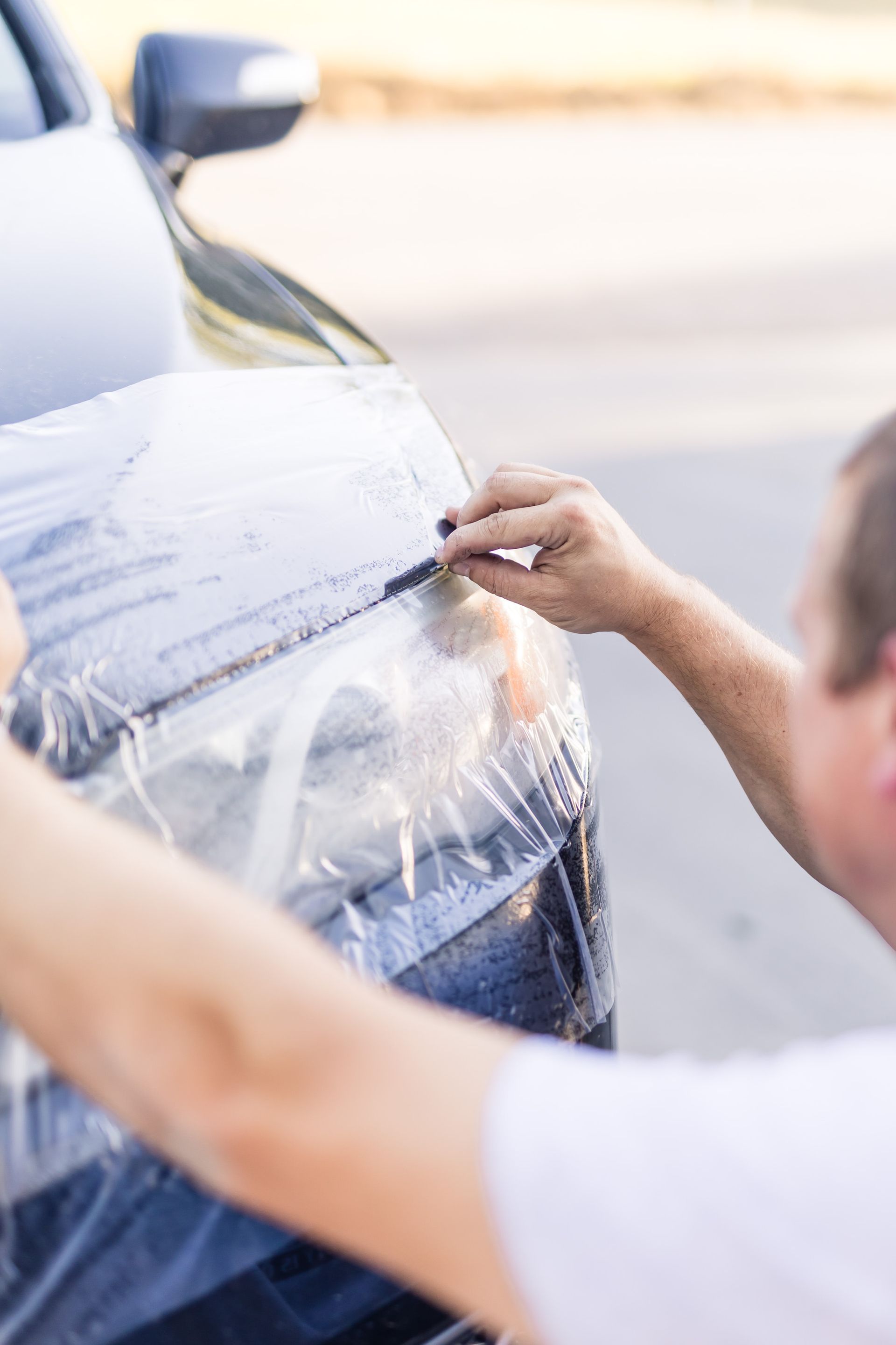 Person applying clear protective film to the headlight of a dark car outdoors.