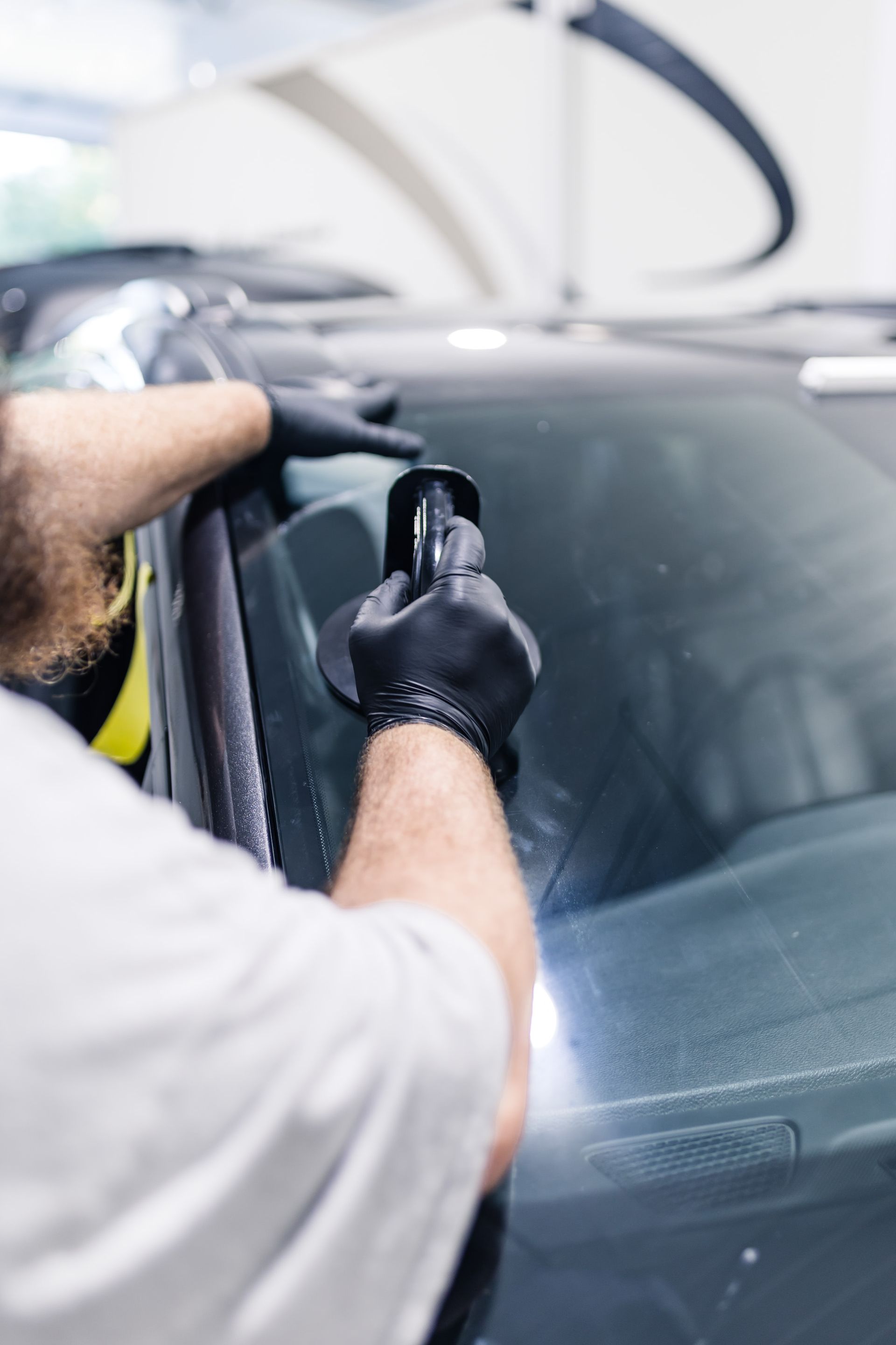 Person wearing black gloves polishing a car windshield with a tool inside a car detailing shop.