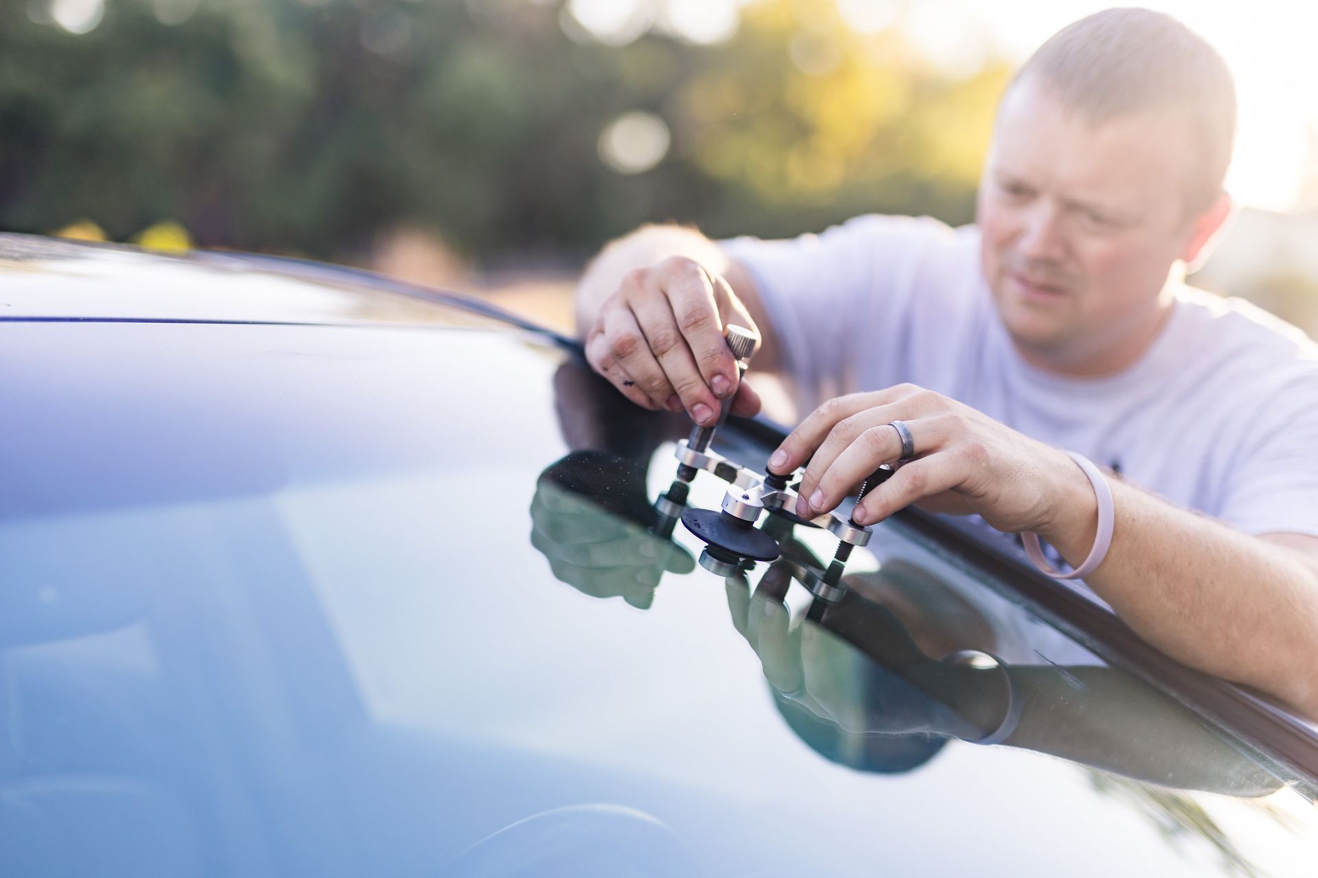 Man in white shirt installing a car roof rack on a dark car, outdoors.