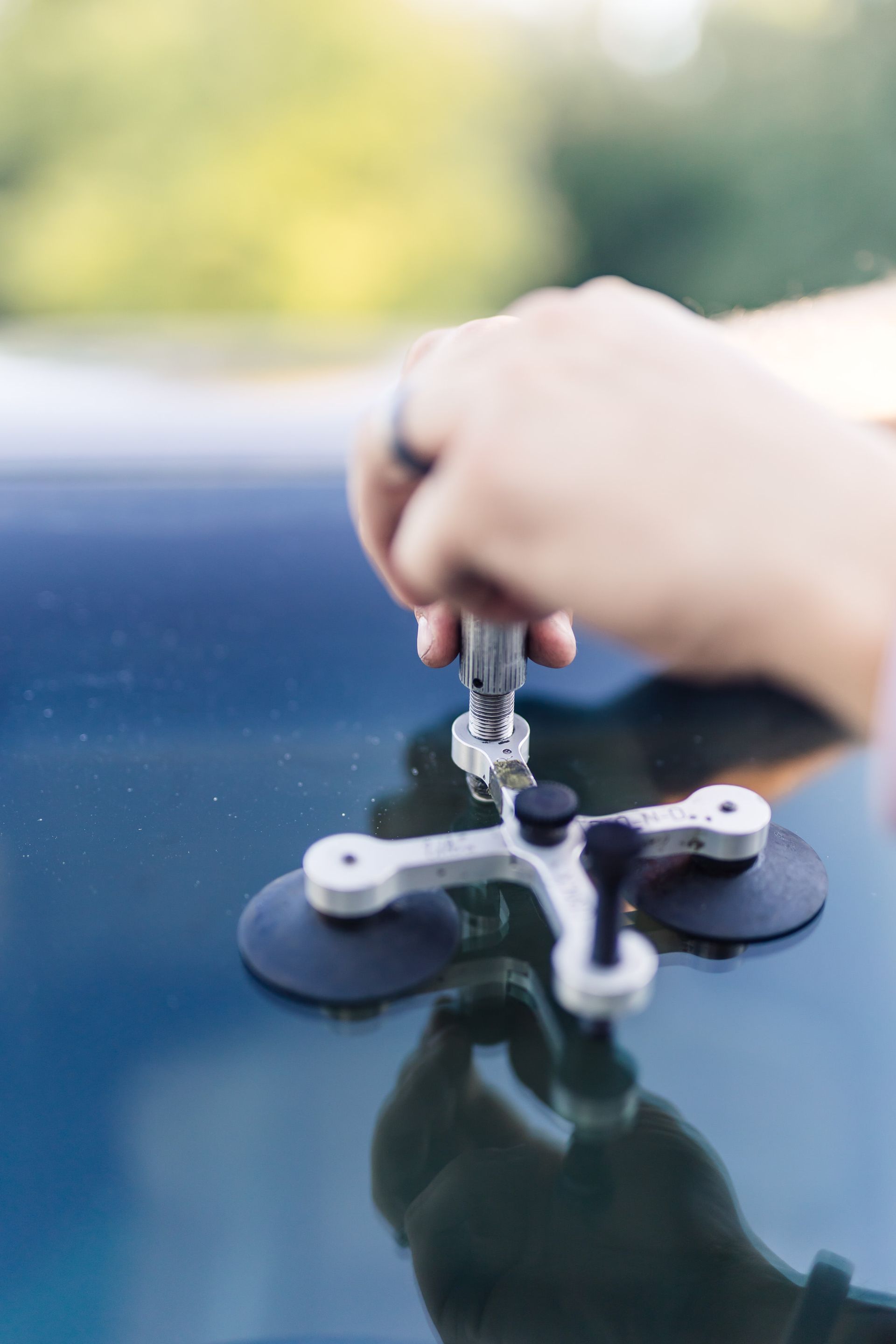 A person repairing a windshield crack with a repair kit. The kit has suction cups and a tool being manipulated.