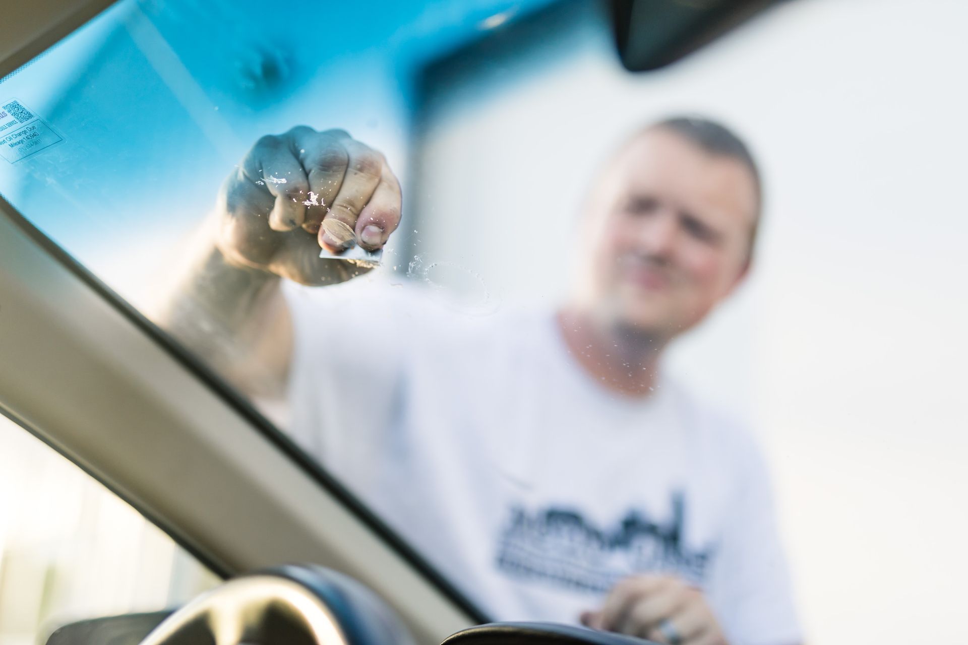 Man cleaning a car windshield with a cloth, blurred background, sunny day.