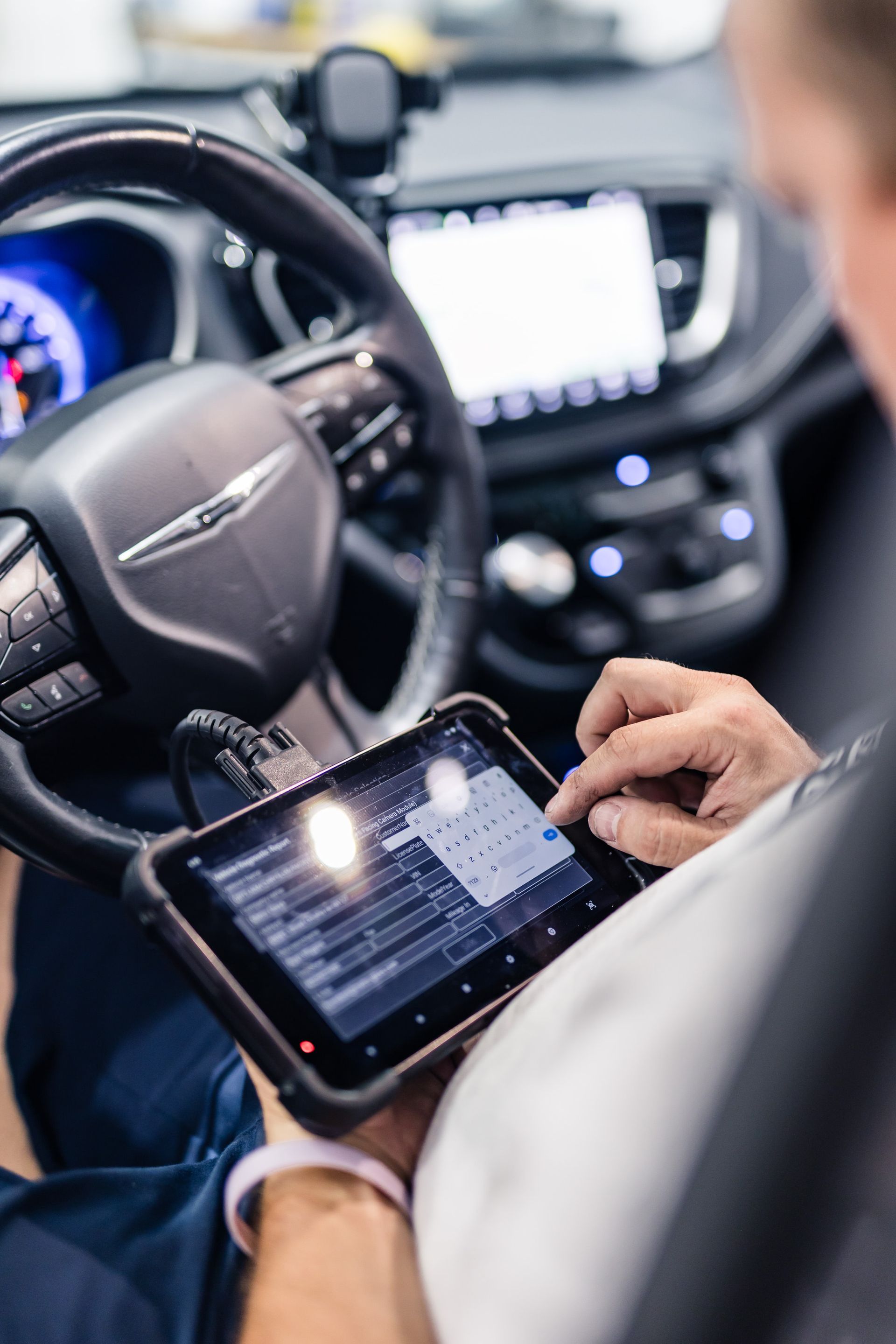 A person using a tablet inside a Chrysler vehicle, likely for diagnostics. They are touching the screen while seated in the driver's seat.