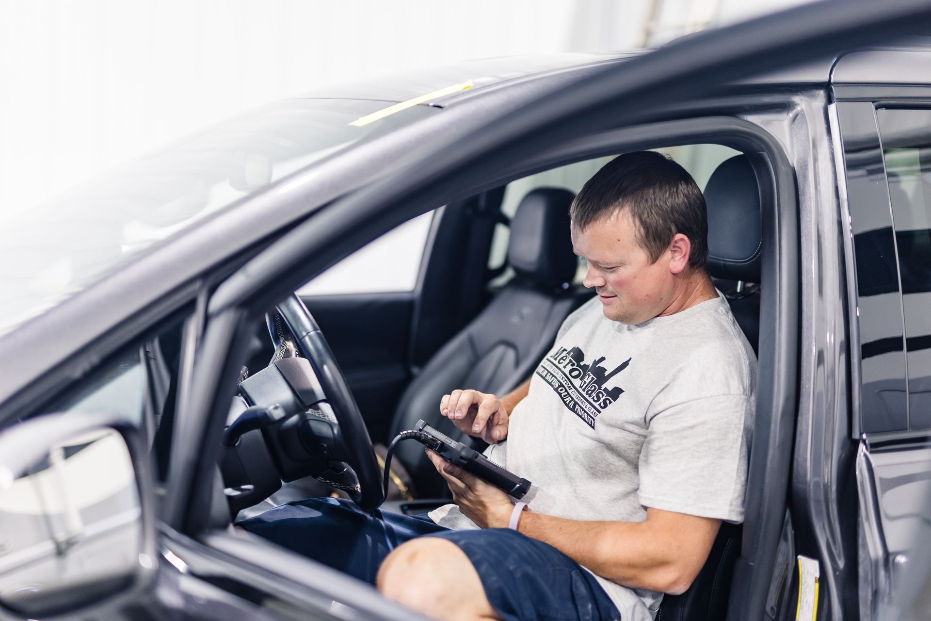 Man in a car, using a diagnostic tool. He's in the driver's seat, looking at the device.