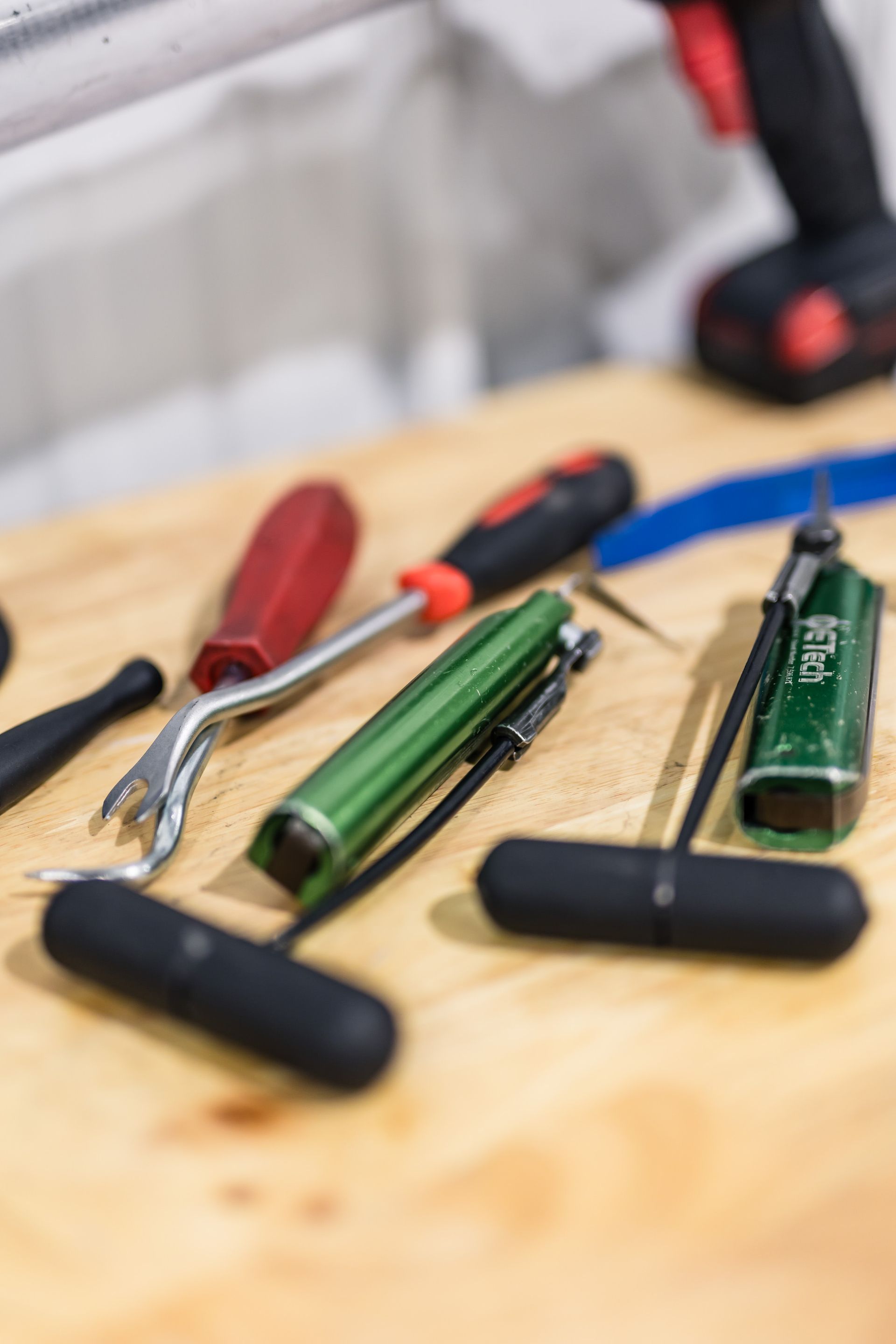 Tools on a wooden surface: a red handle trim tool, green tool, black T-handles, and a screwdriver.