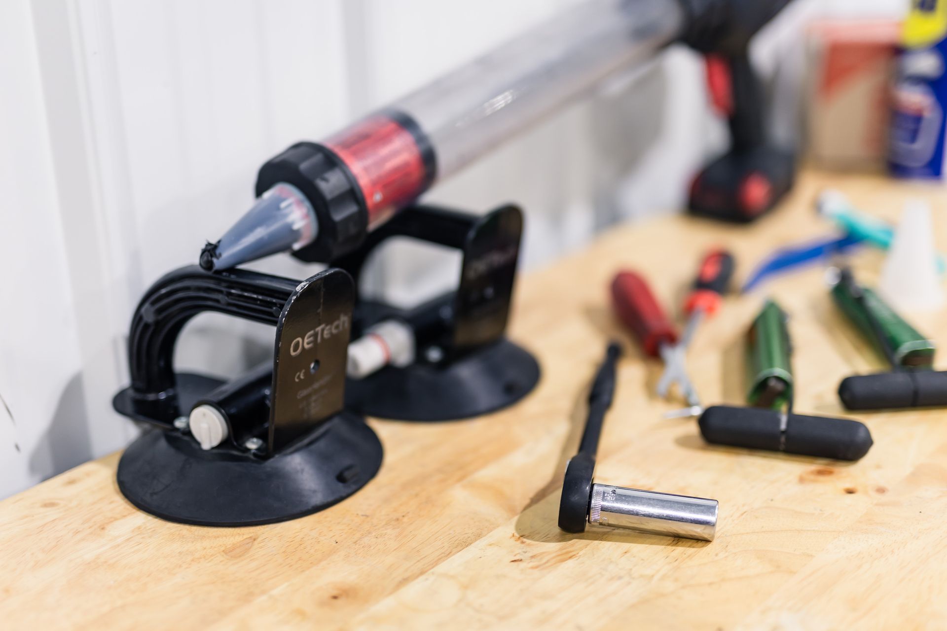 A close-up of tools on a wooden surface: a caulk gun, suction cups, and various hand tools.