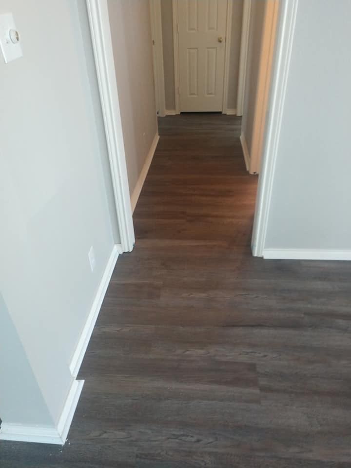 A hallway with a wooden floor and white trim leading to a door.