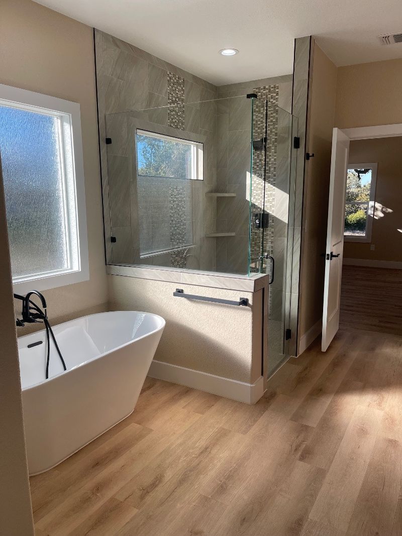 A bathroom with a tub , shower , mirror and window.