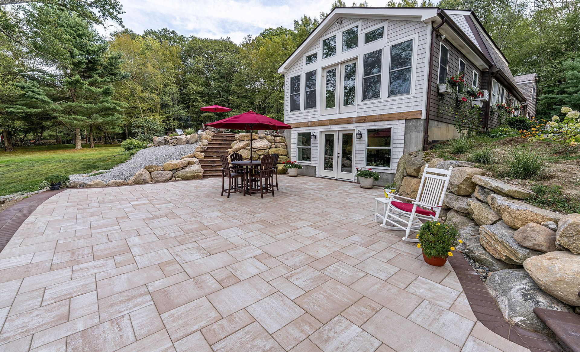 Patio with stone pavers, table and chairs, and a house with large windows.