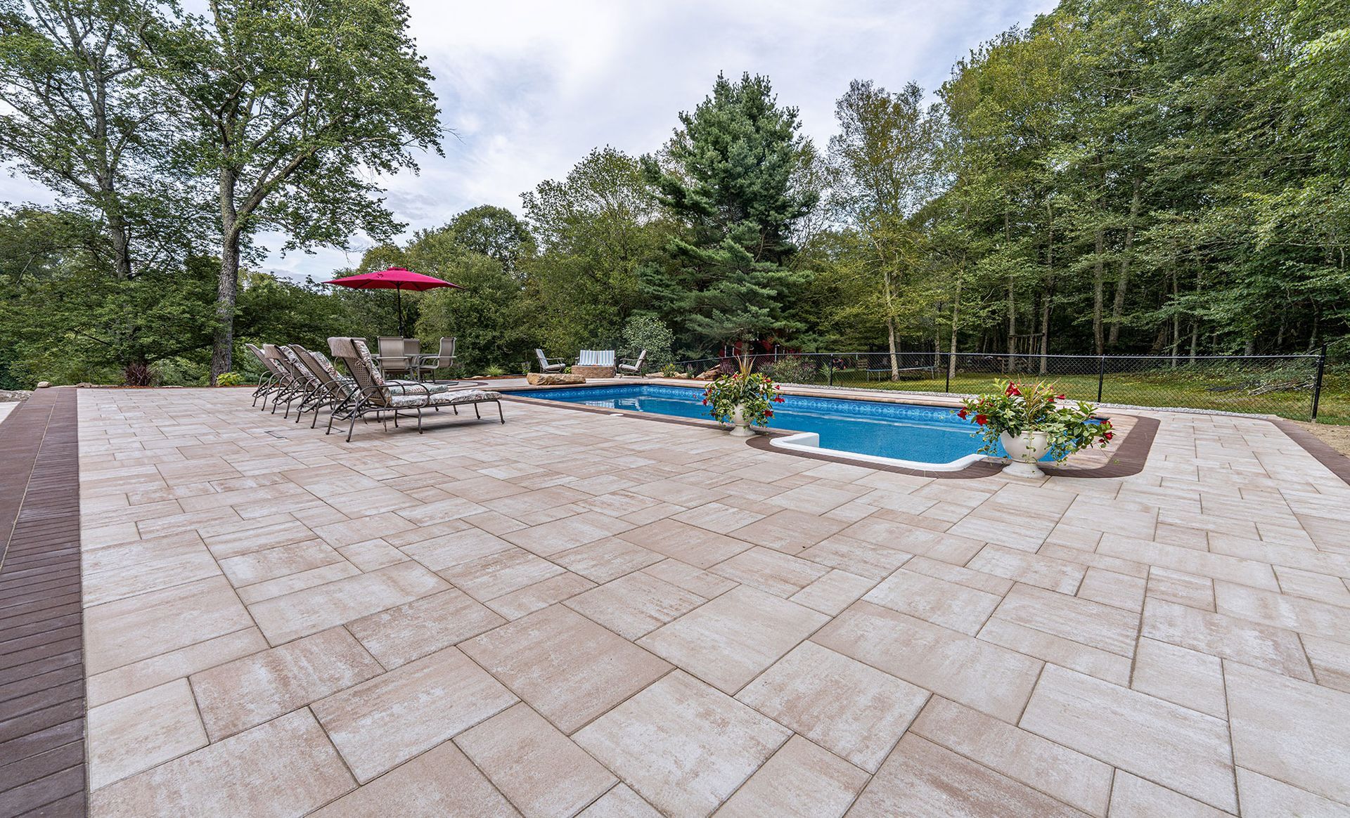 Large stone patio surrounds a swimming pool with lounge chairs and trees in the background.