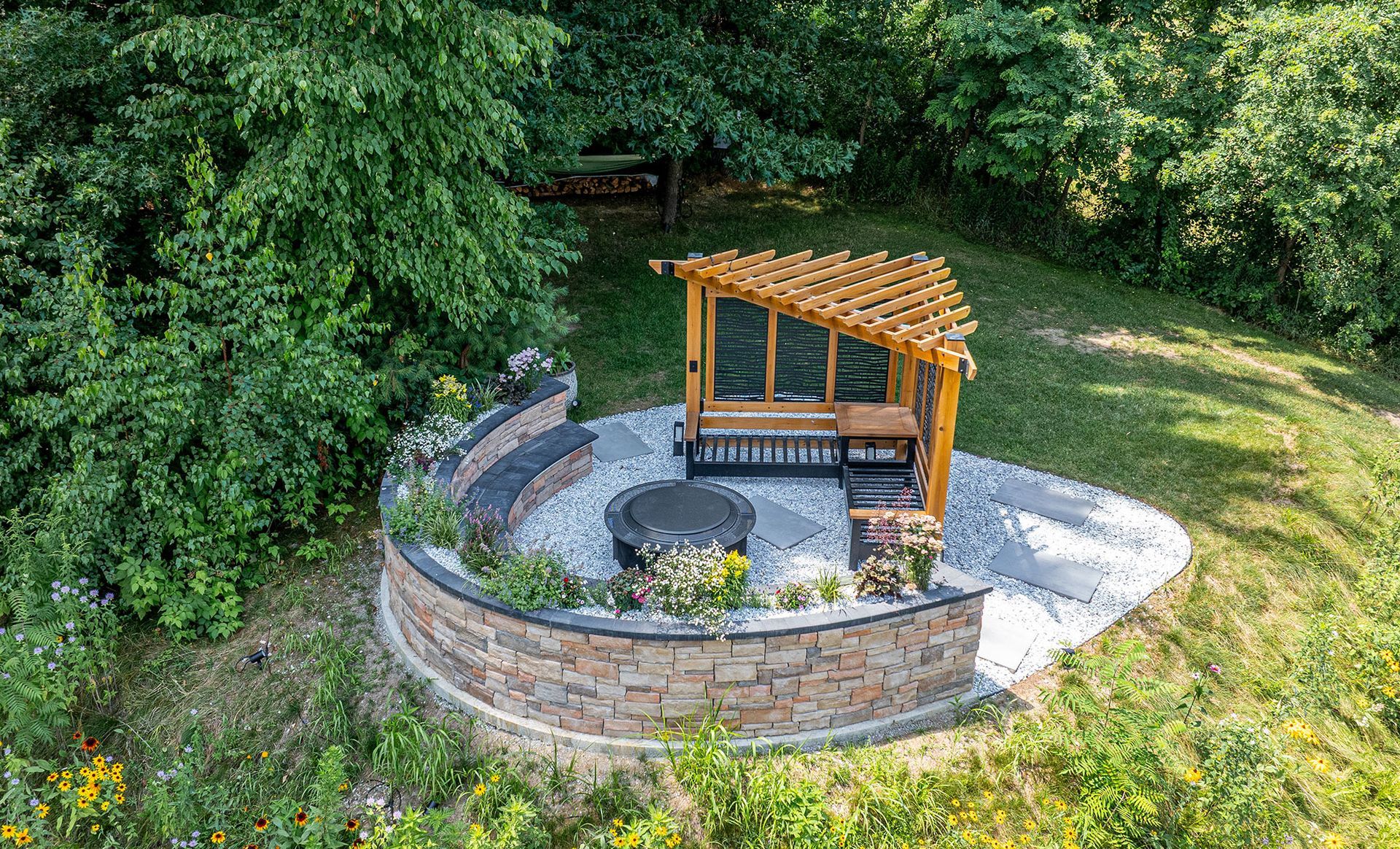 Outdoor seating area with a wooden pergola, fire pit, and curved stone wall.
